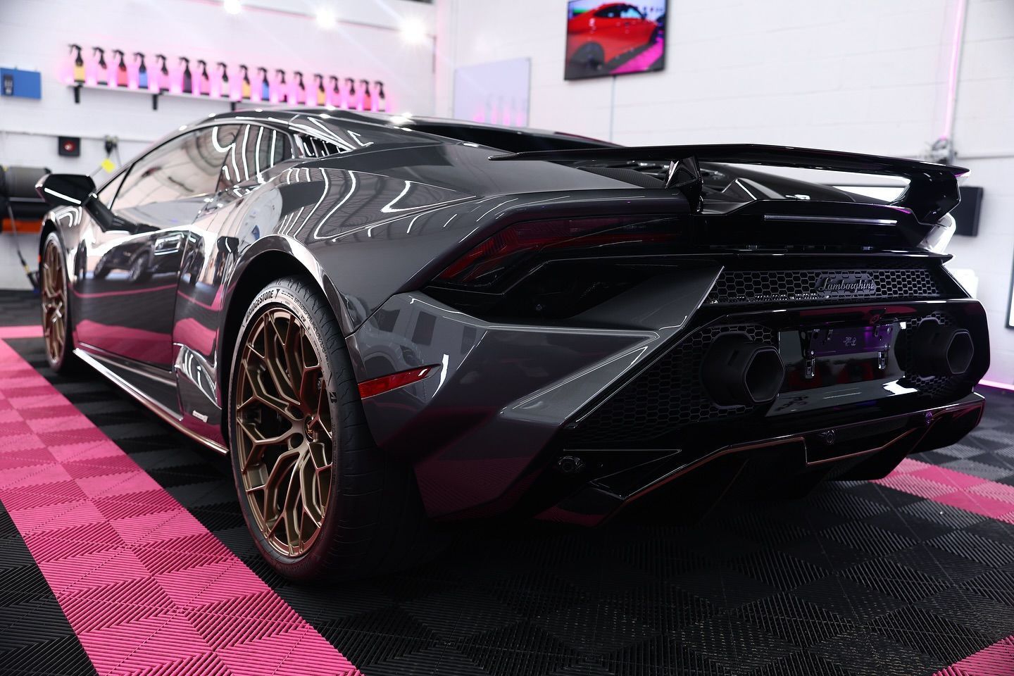 Dark grey Lamborghini Huracan with bronze wheels, parked on a pink and black tiled floor.