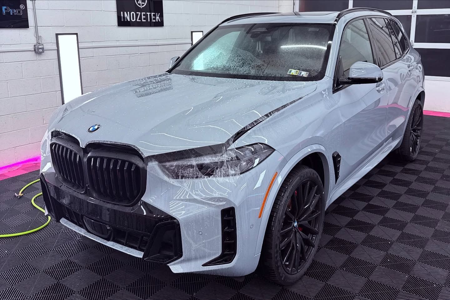Light blue BMW SUV in a garage, black wheels and trim, wet surface.