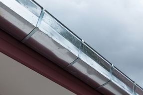 A close up of a metal gutter on a roof with a cloudy sky in the background.