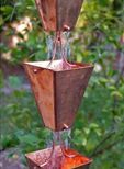 A close up of a copper rain chain with water coming out of it.