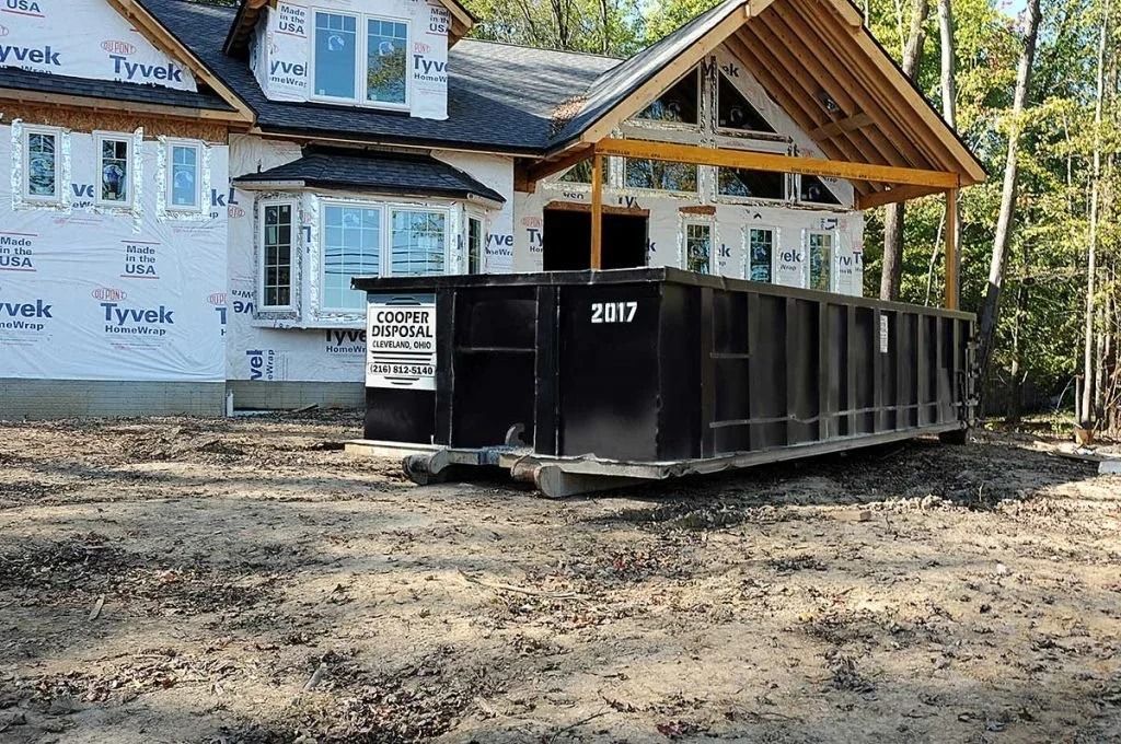 Black dumpster in front of a house under construction.