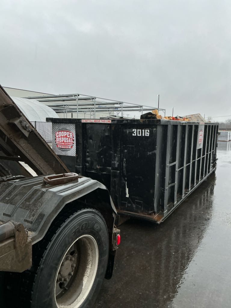 Construction site with black dumpsters, dirt ground, and blue sky. A safety cone is in the foreground.