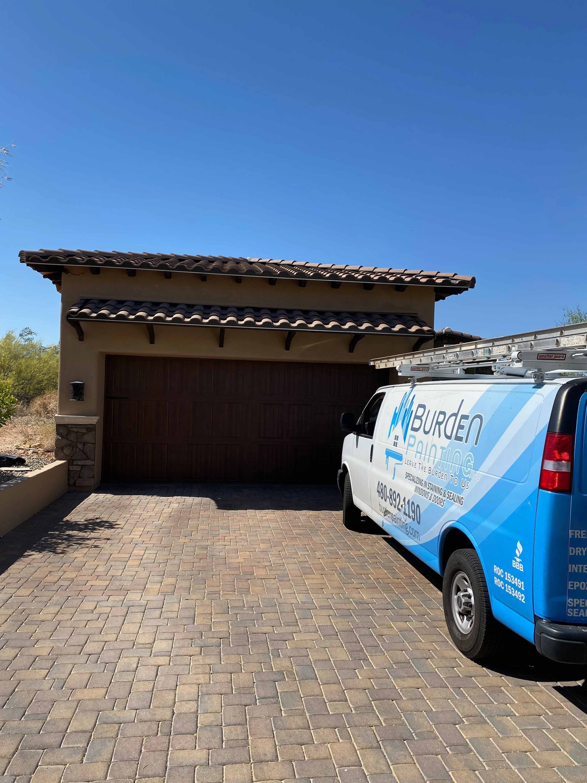 A blue and white van is parked in front of a garage door.