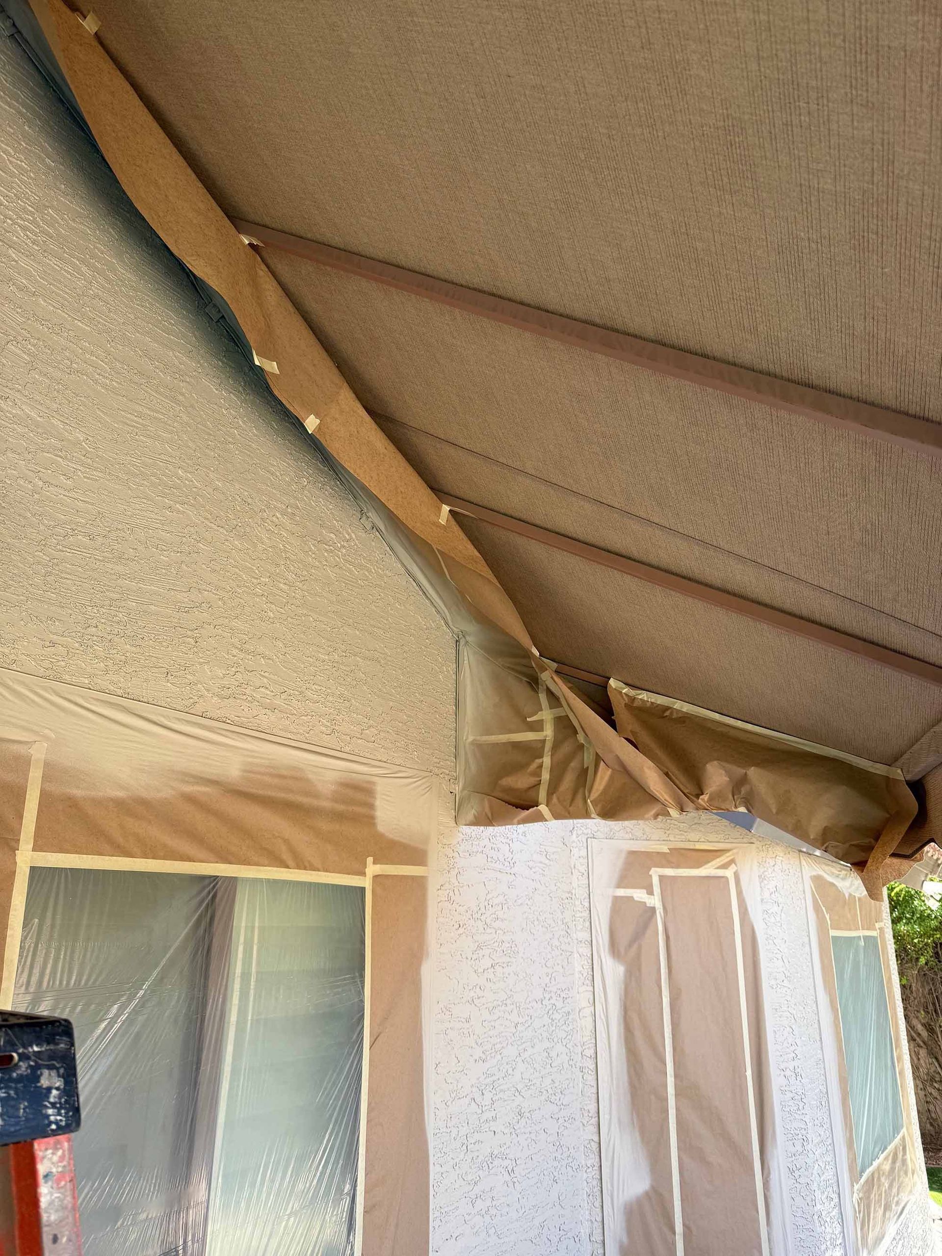 A ceiling is being painted in a room with a ladder in the foreground