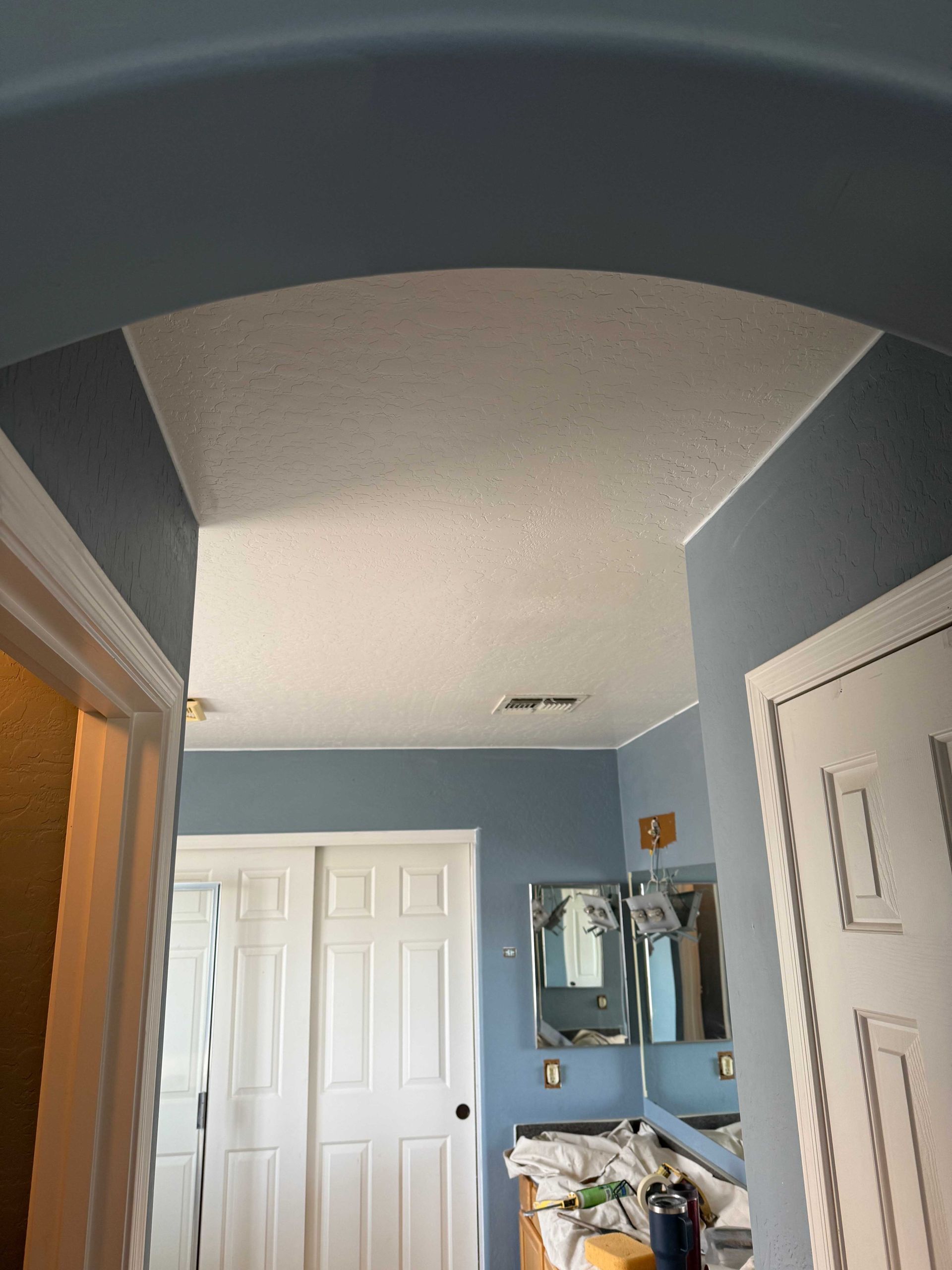 A bathroom with blue walls , white doors , a sink and a mirror.