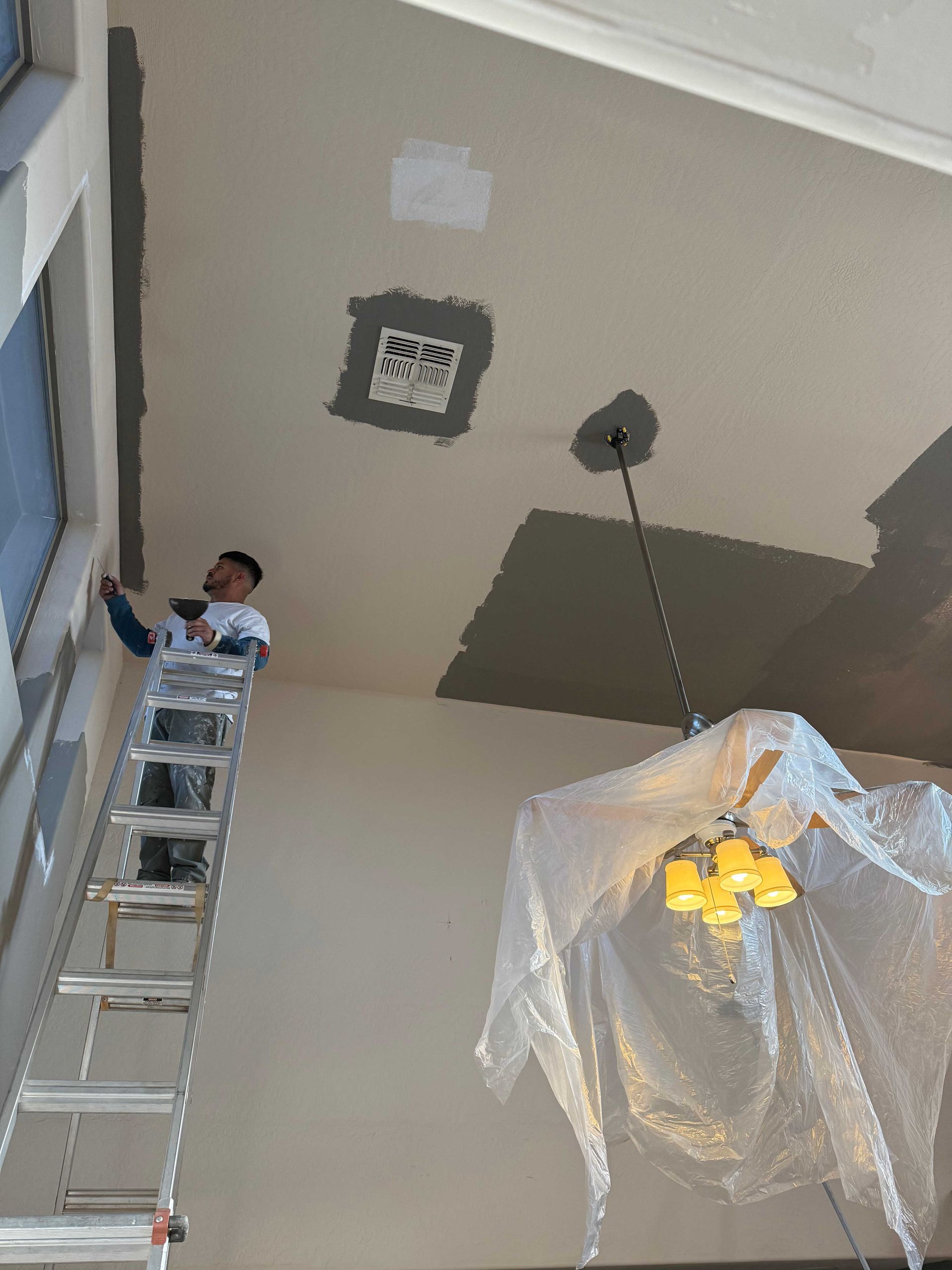 A man on a ladder is painting the ceiling of a room