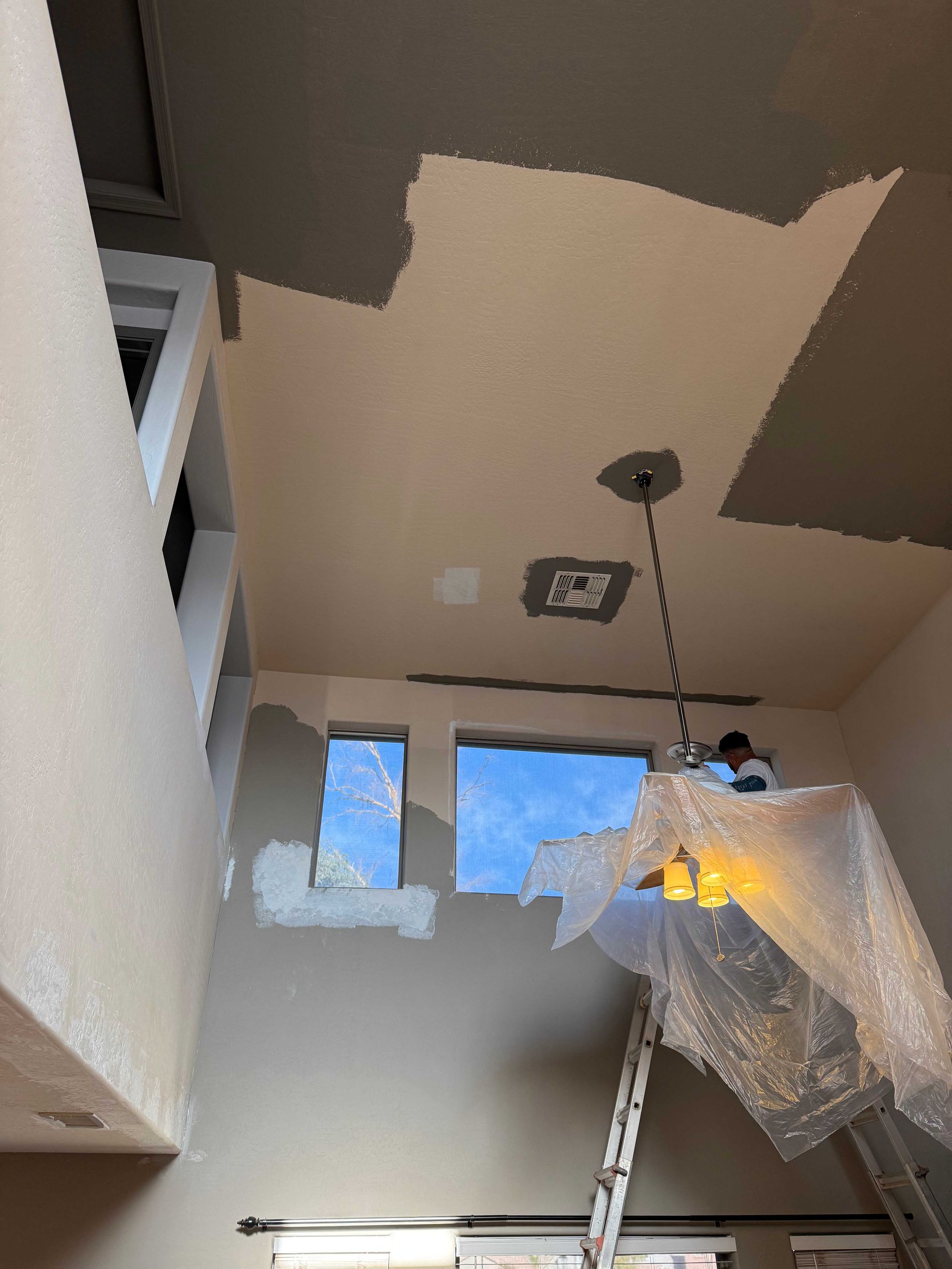 A person is painting the ceiling of a room with a ladder.