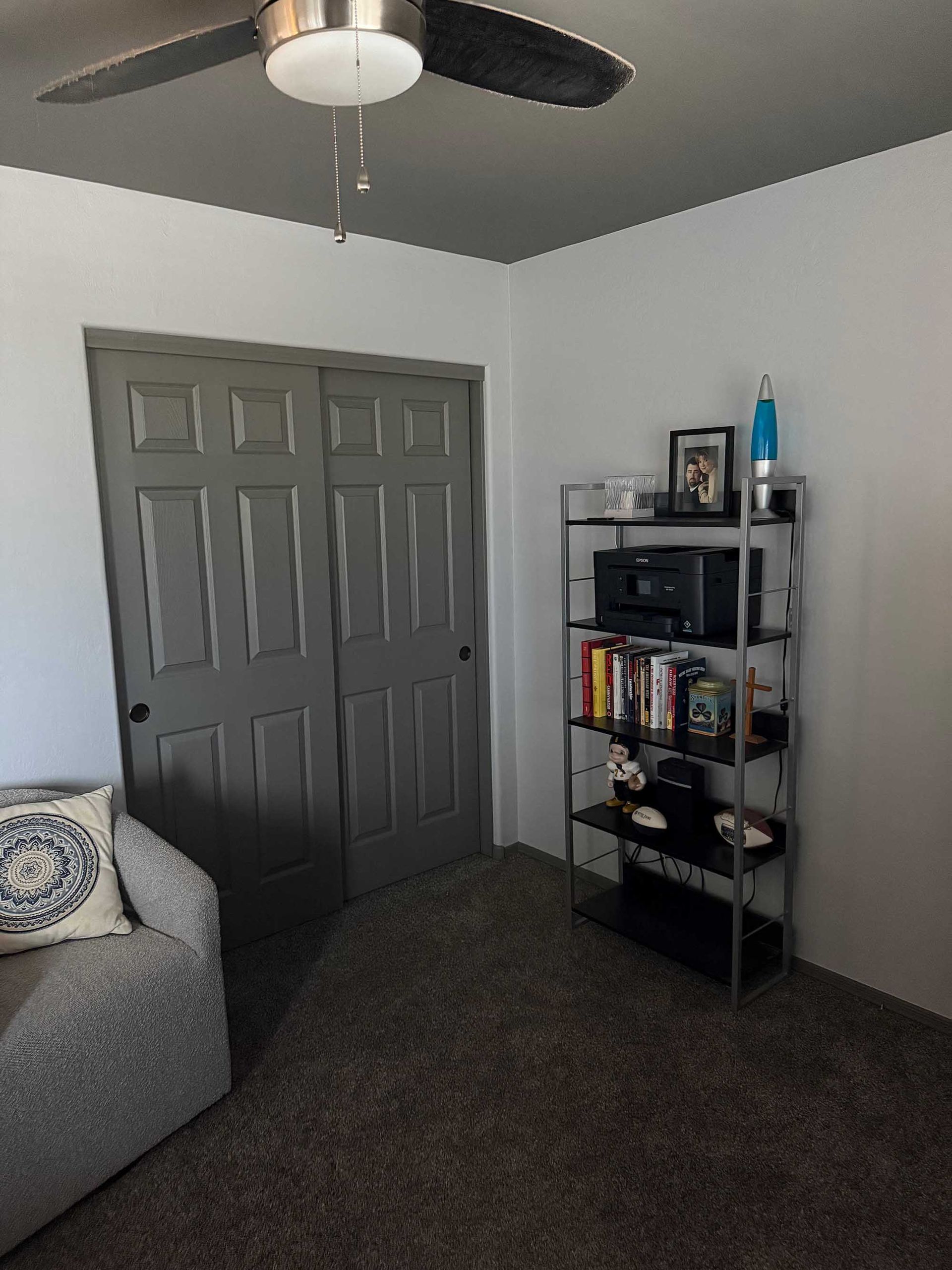 A living room with a ceiling fan and a bookshelf.