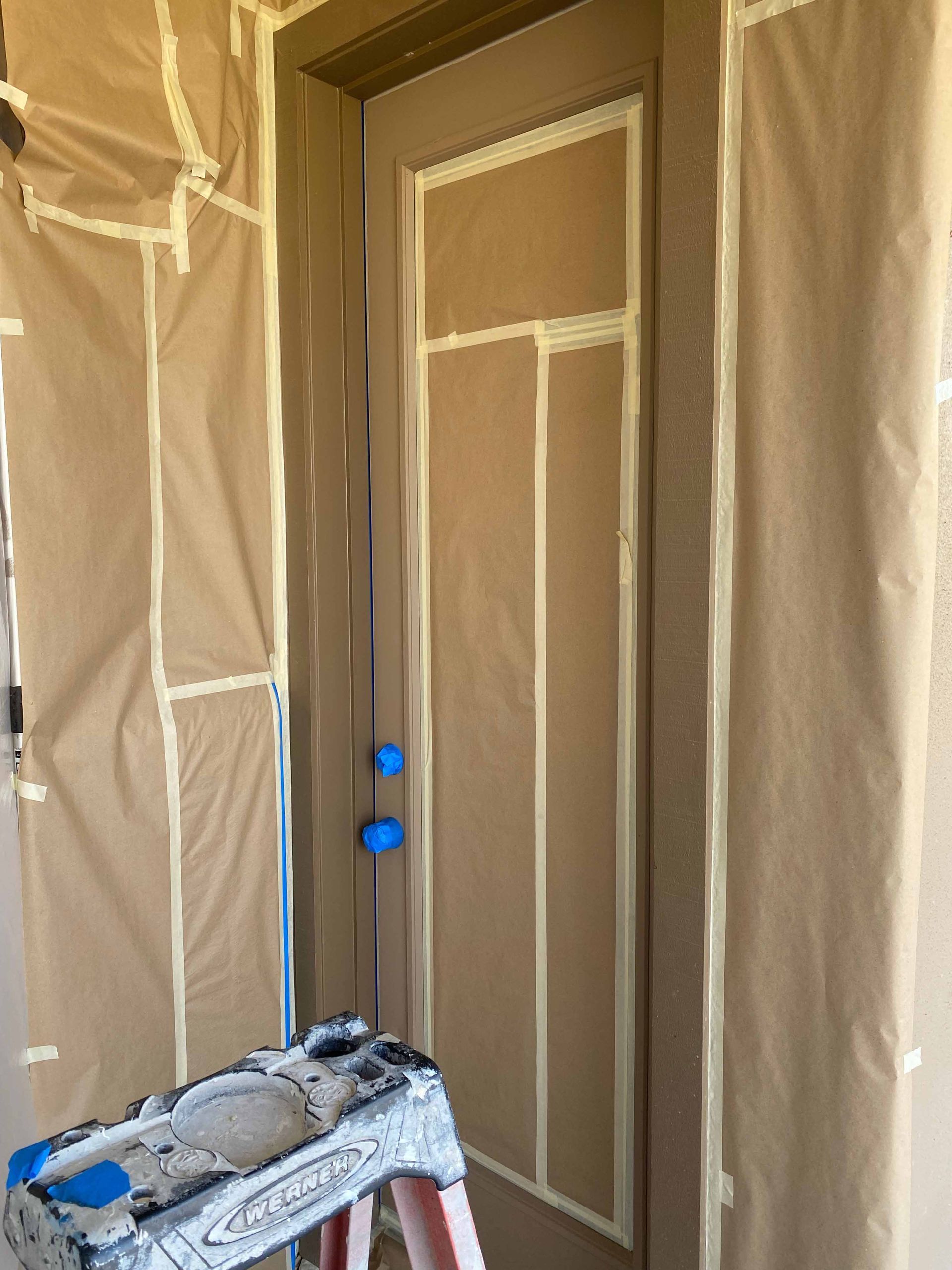 A door is being painted in a room with a ladder.