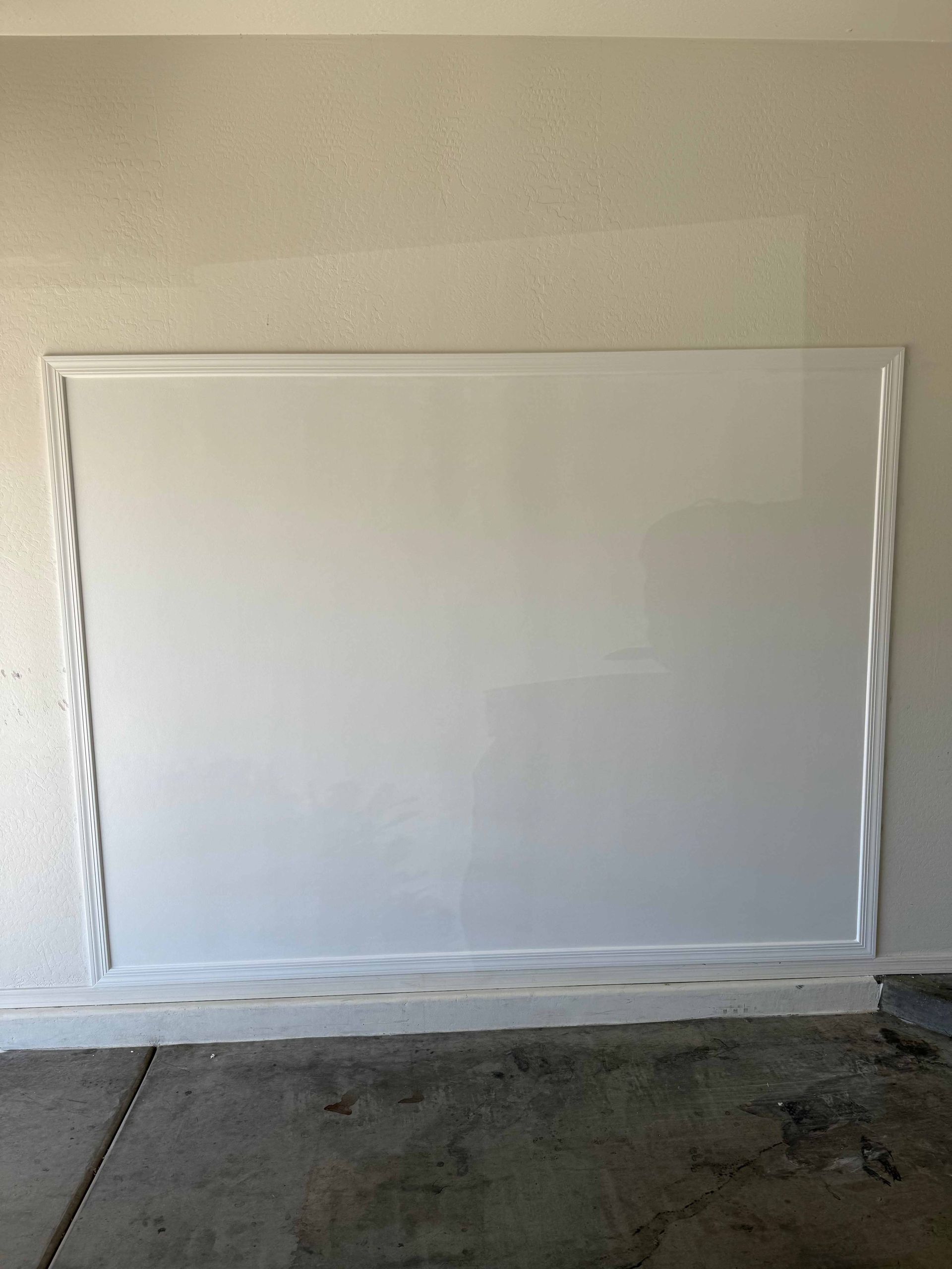 A large white board is hanging on a wall in a garage.
