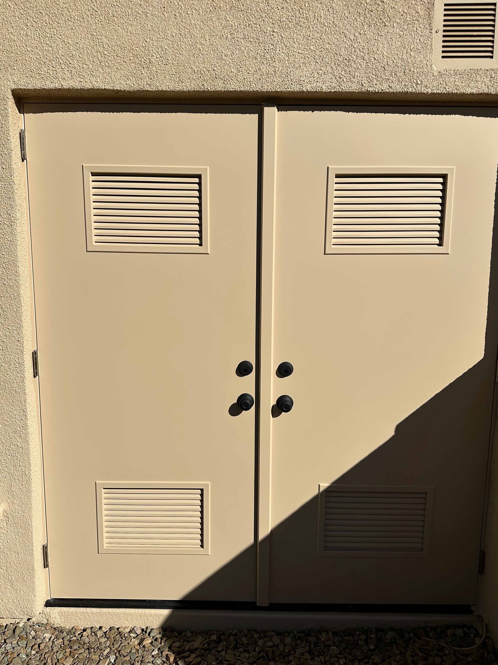 A pair of doors with ventilation holes on the side of a building.