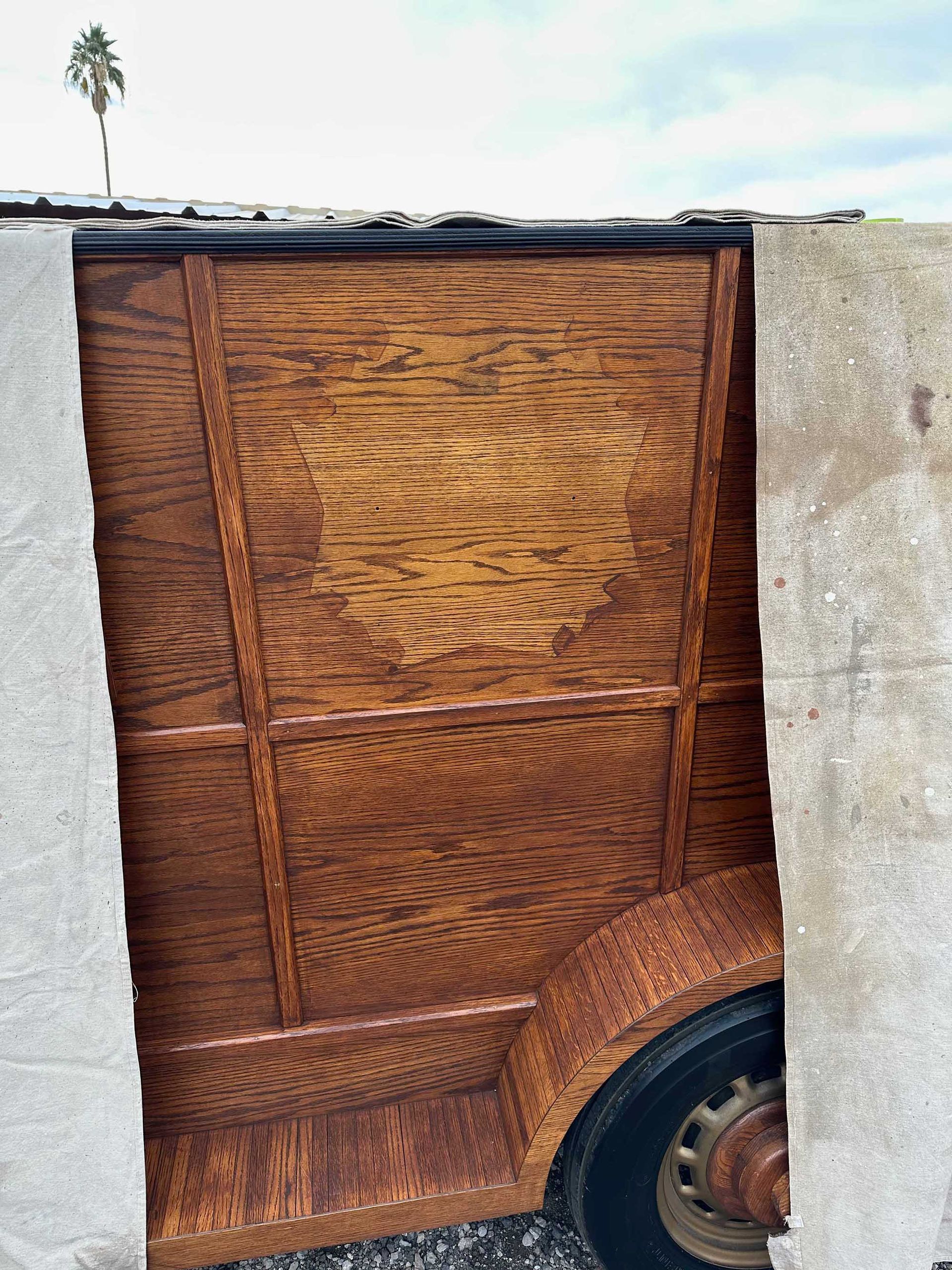A close up of a wooden trailer with a palm tree in the background.