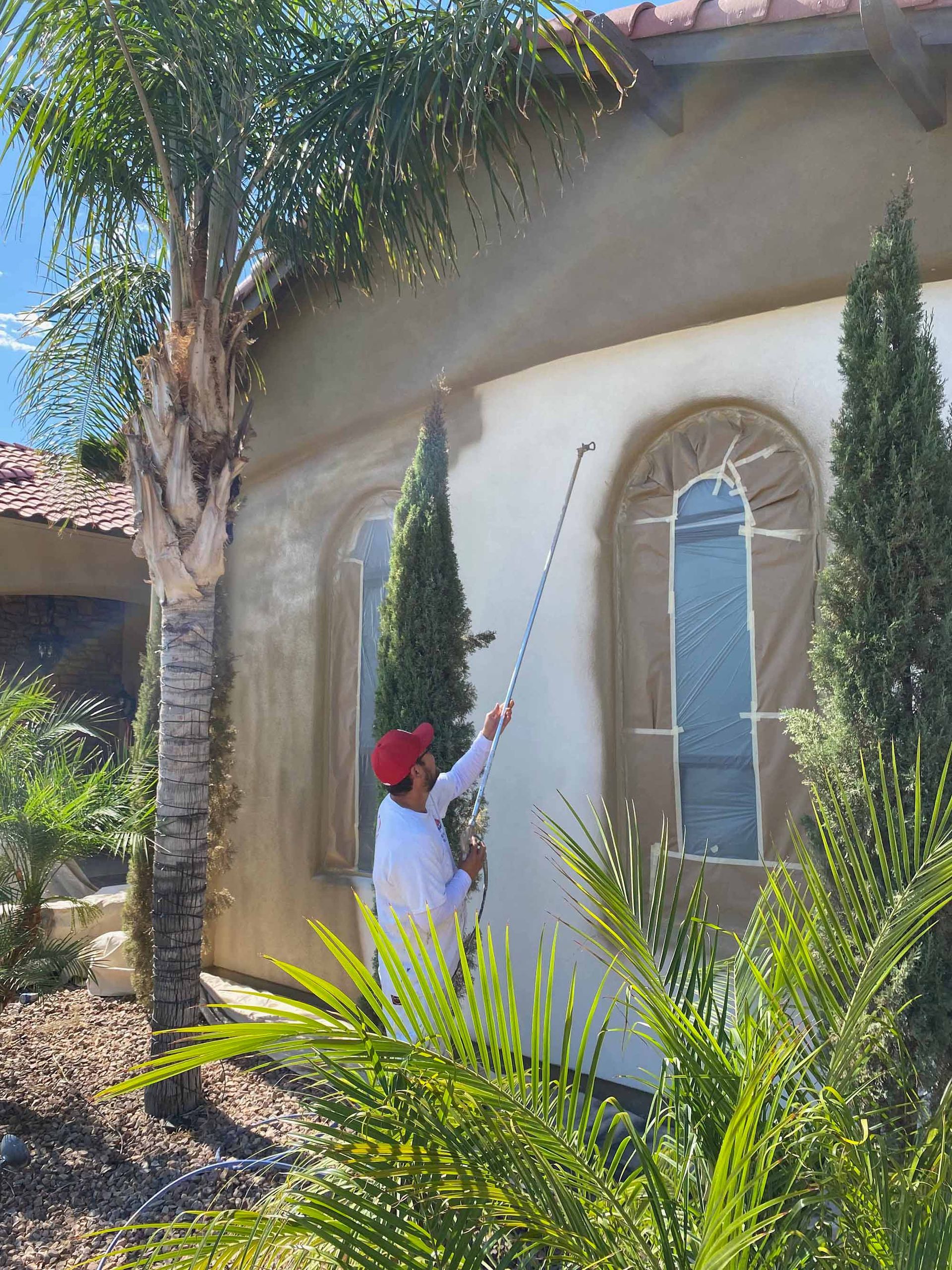 A man is spraying paint on the side of a house.
