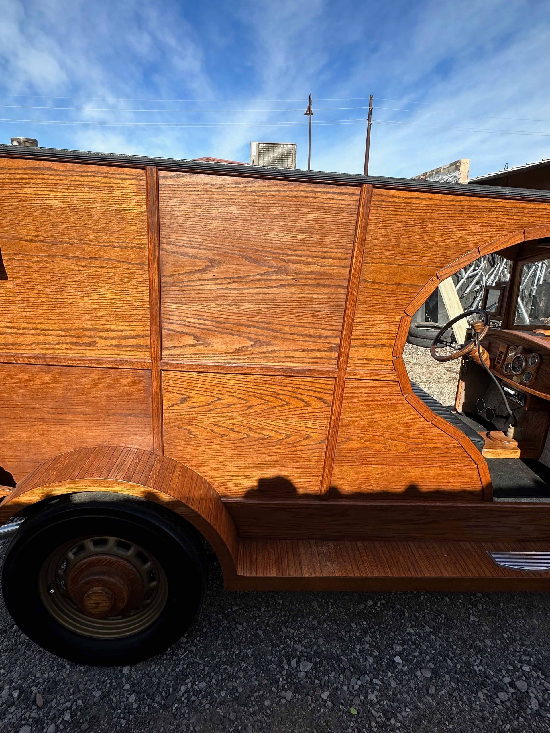 A wooden van with a round window is parked on gravel.