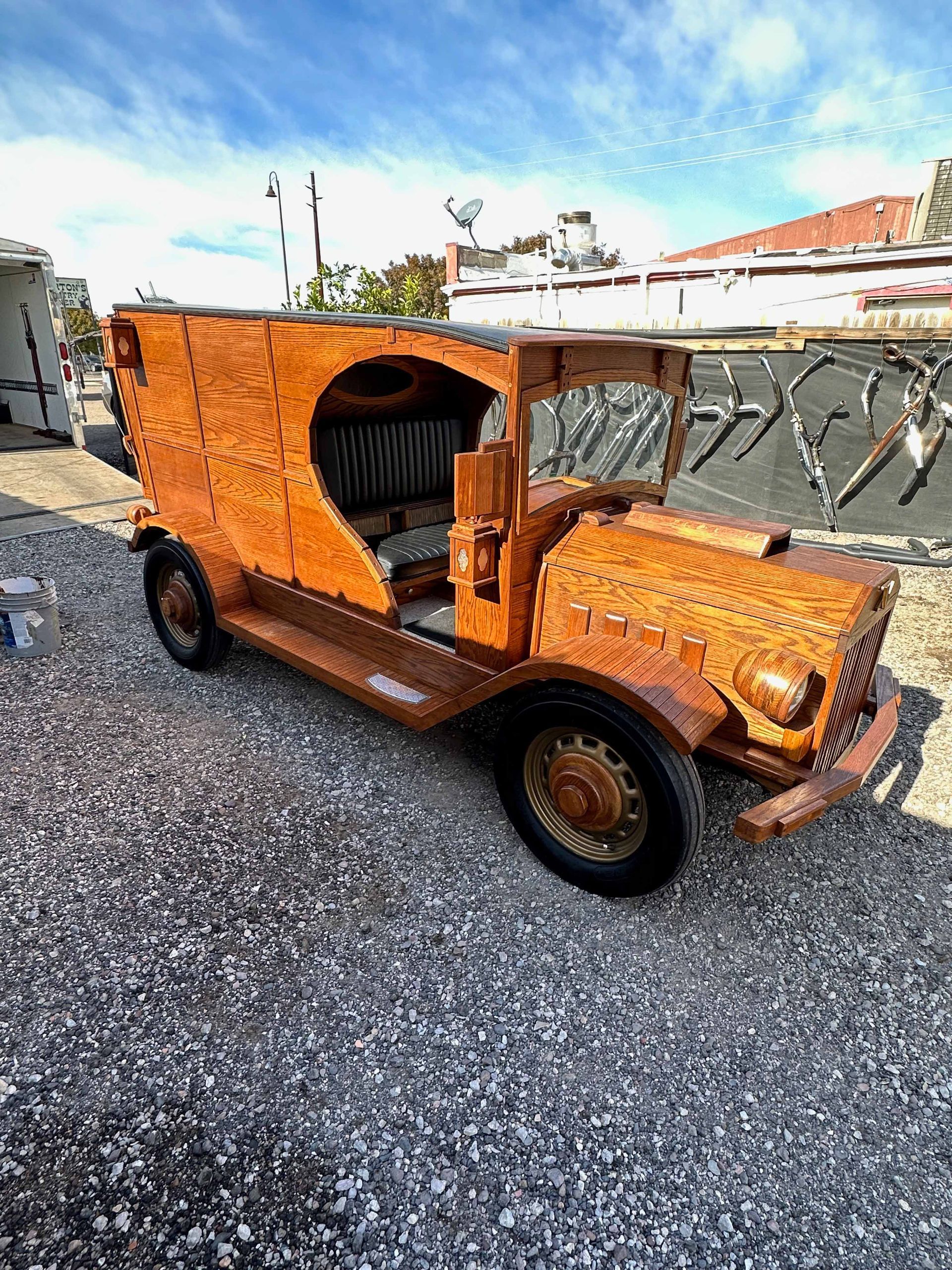 A wooden car is parked in a gravel lot.