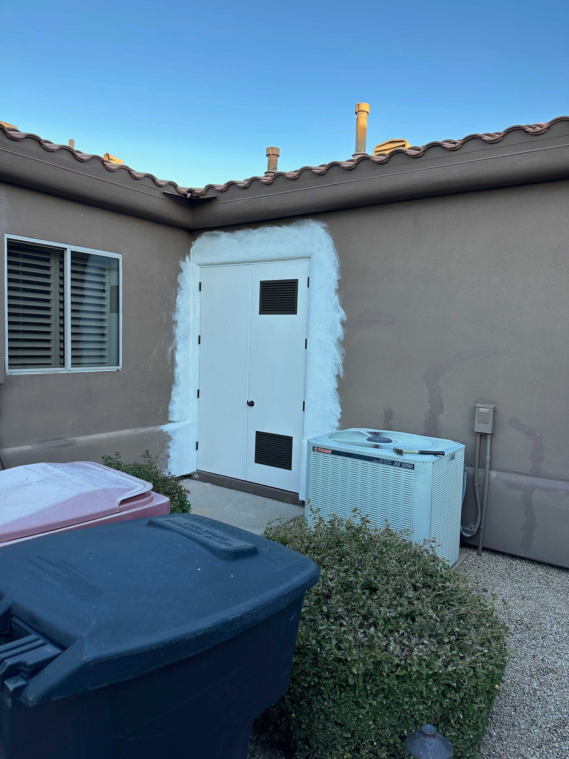A house with a white door and a black trash can in front of it.