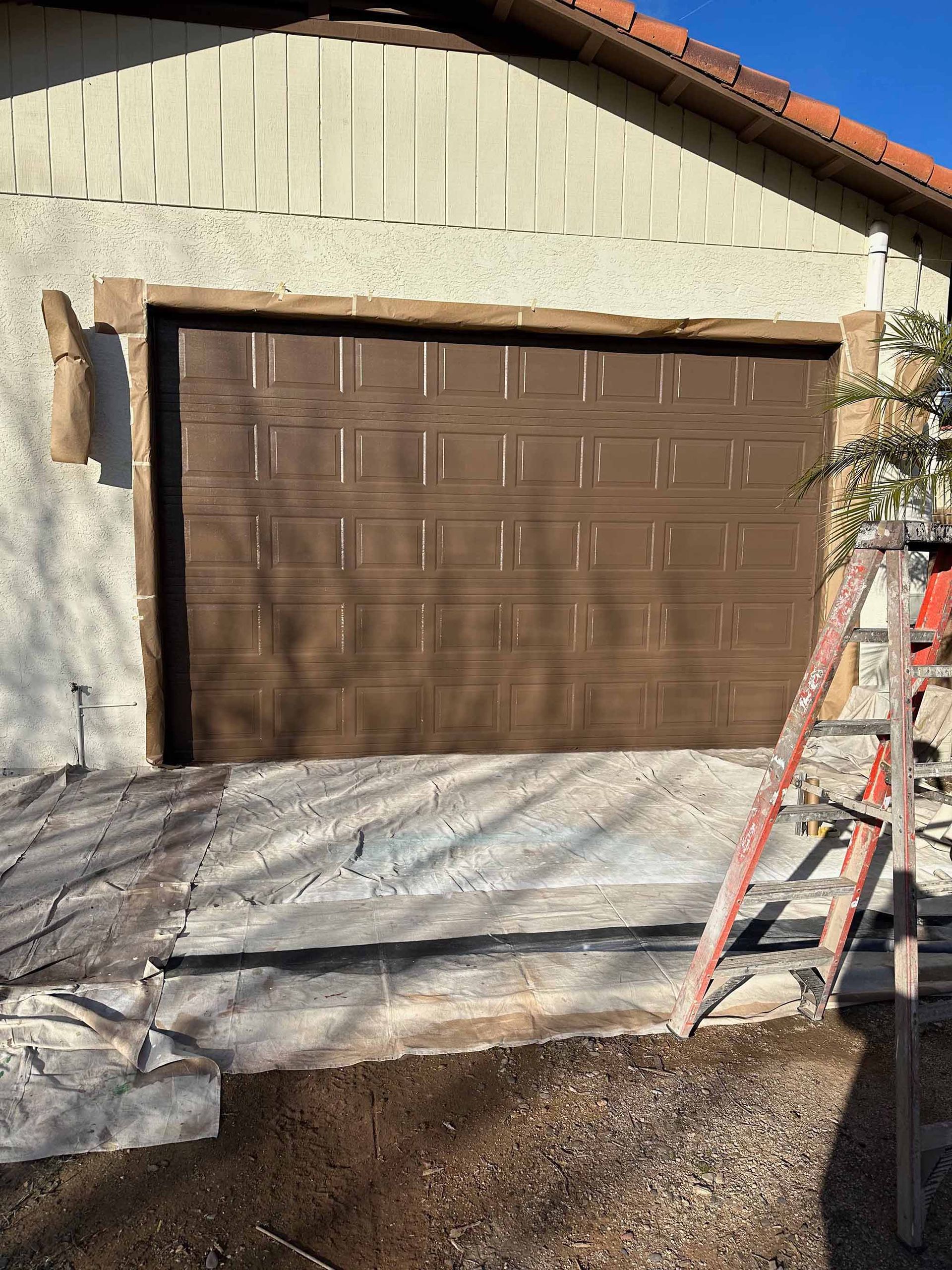 A brown garage door is being painted in front of a house.