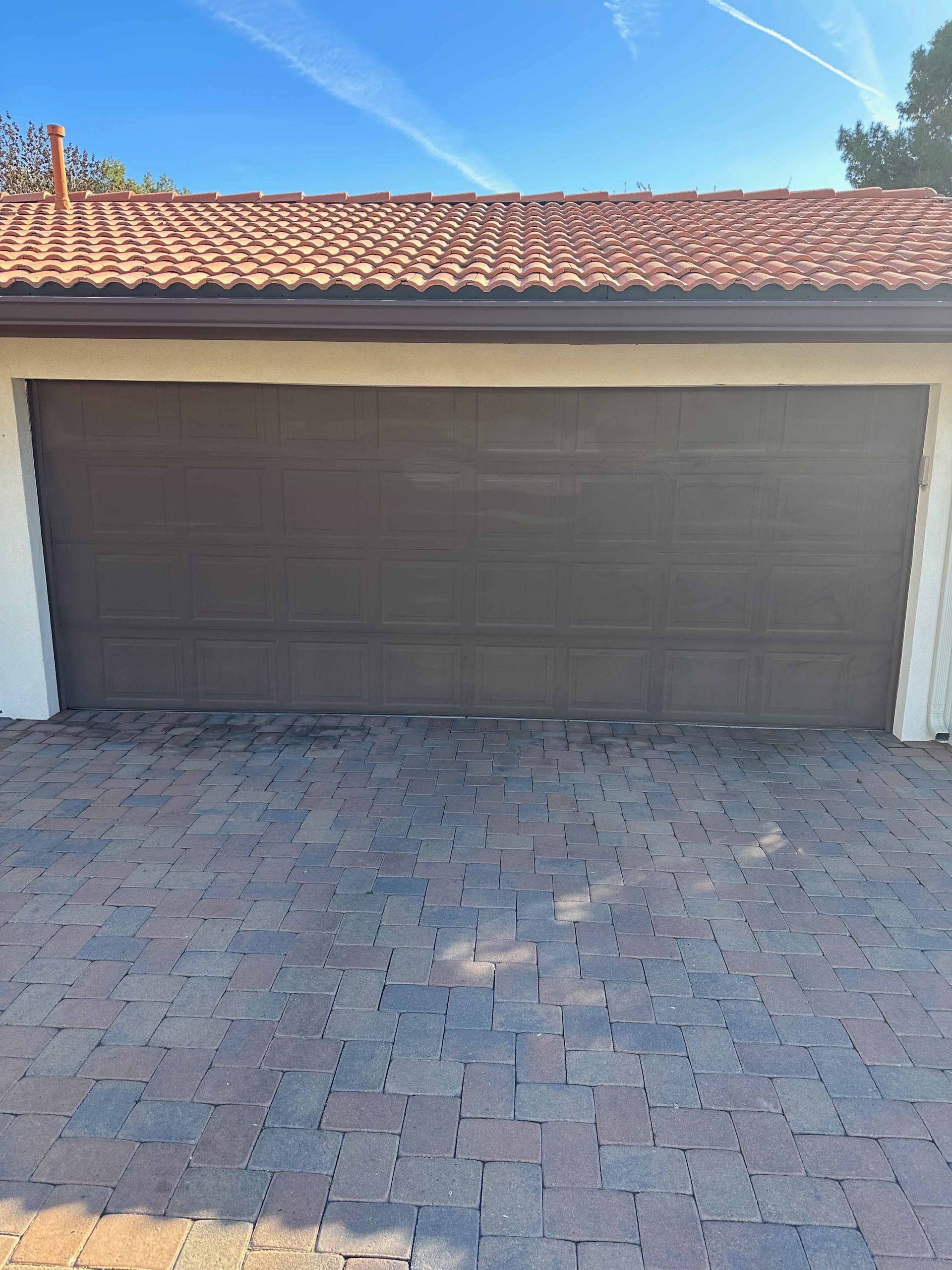 A garage door with a tiled roof is sitting on a brick driveway.