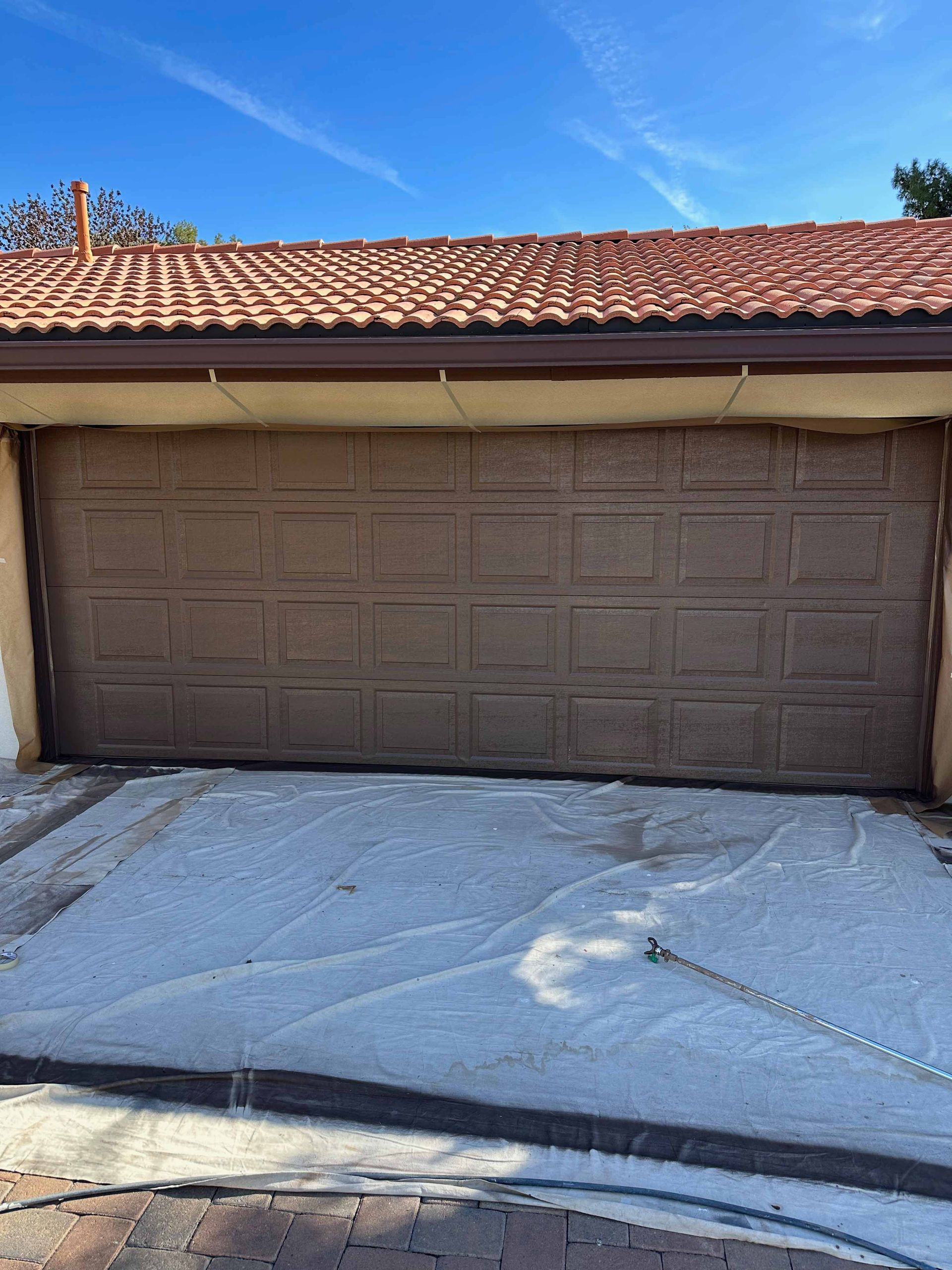 A brown garage door is being painted in front of a house.