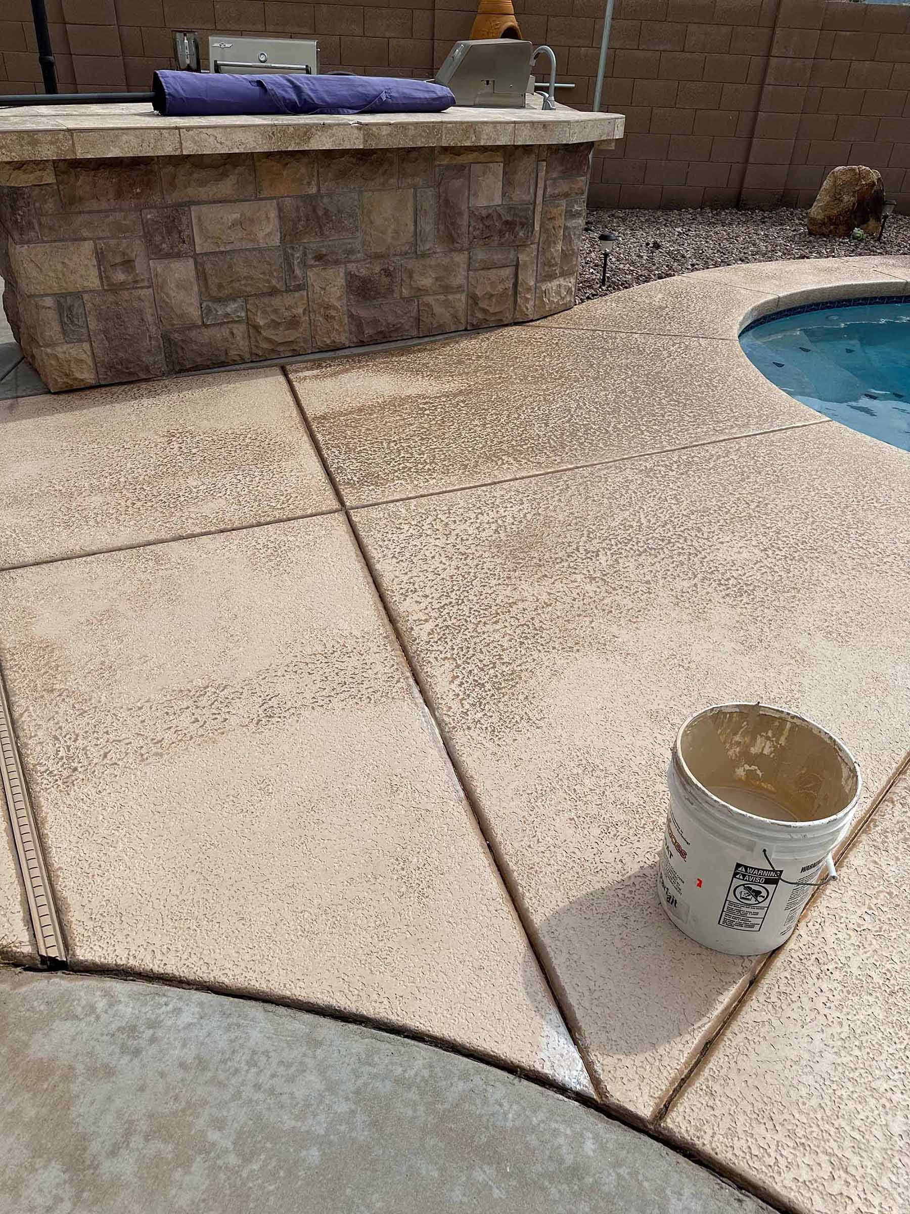 A bucket is sitting on a patio next to a pool.