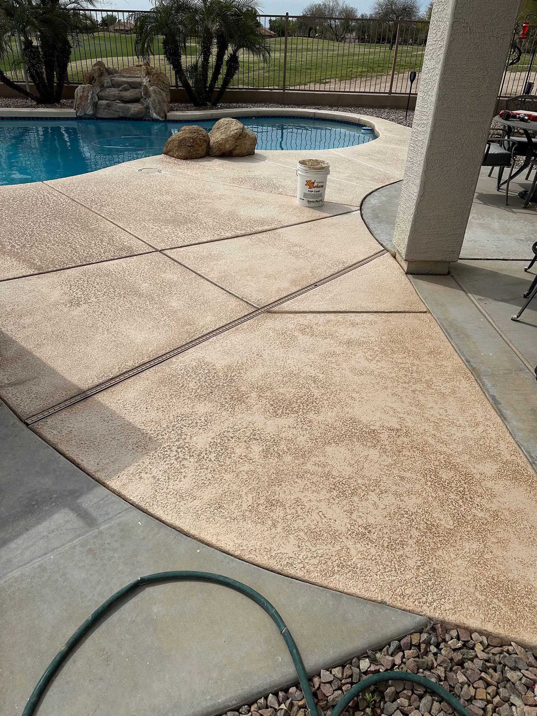 A hose is sitting on the side of a patio next to a pool.