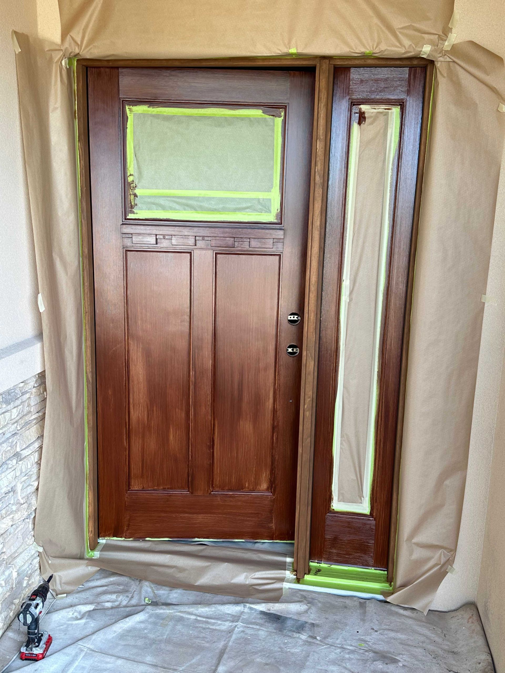 A wooden door is being painted with a green tape covering it.