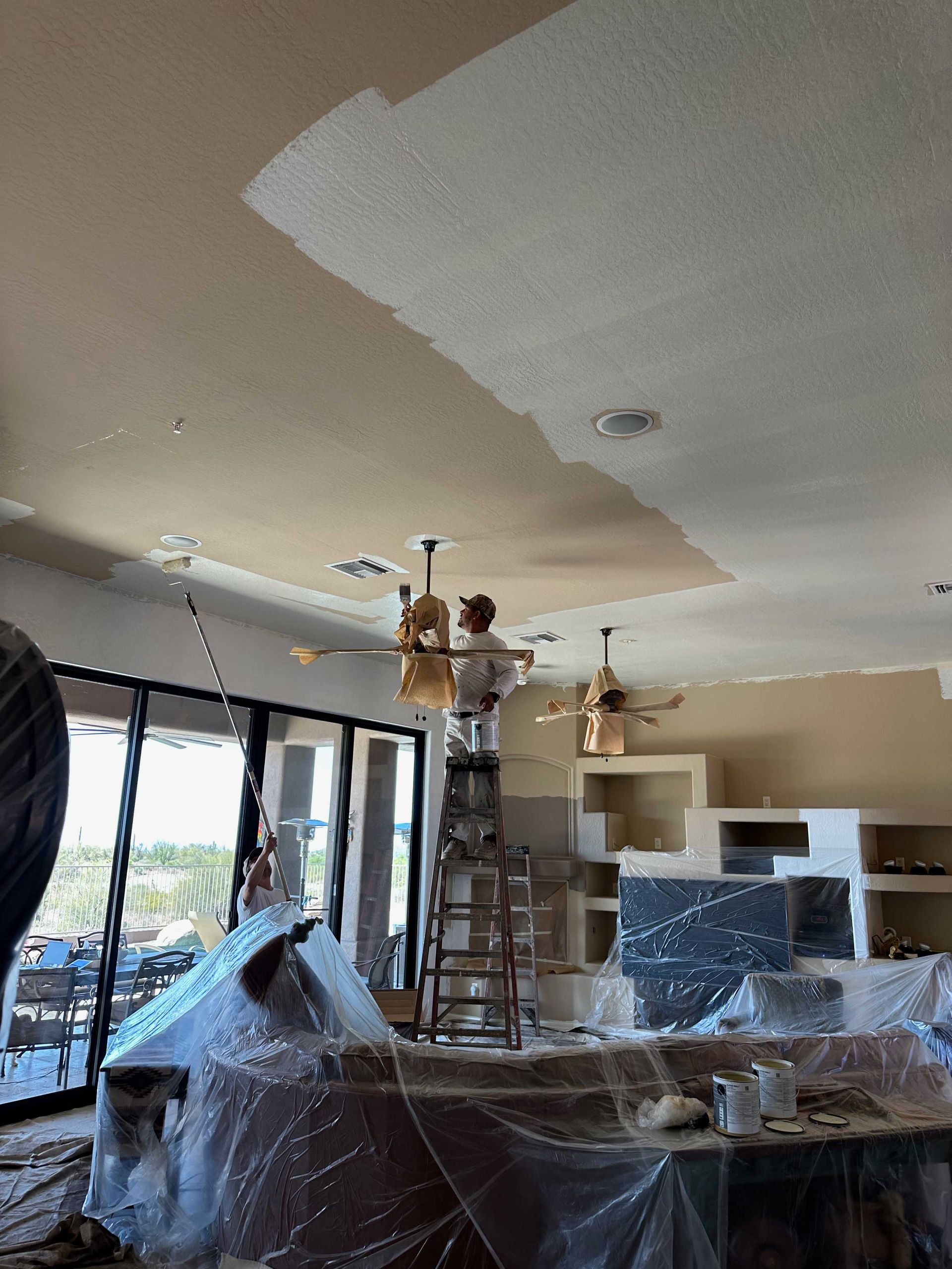 A man on a ladder is painting the ceiling of a living room.