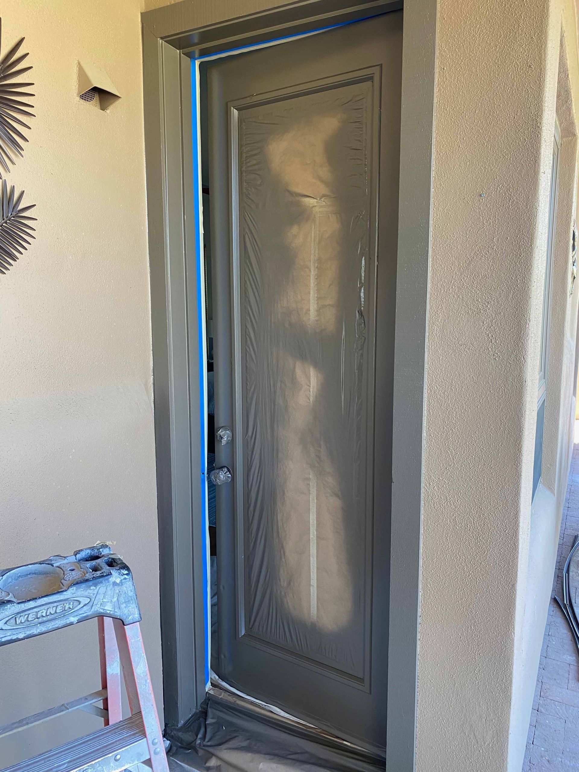 A door is being painted on a wall next to a ladder.