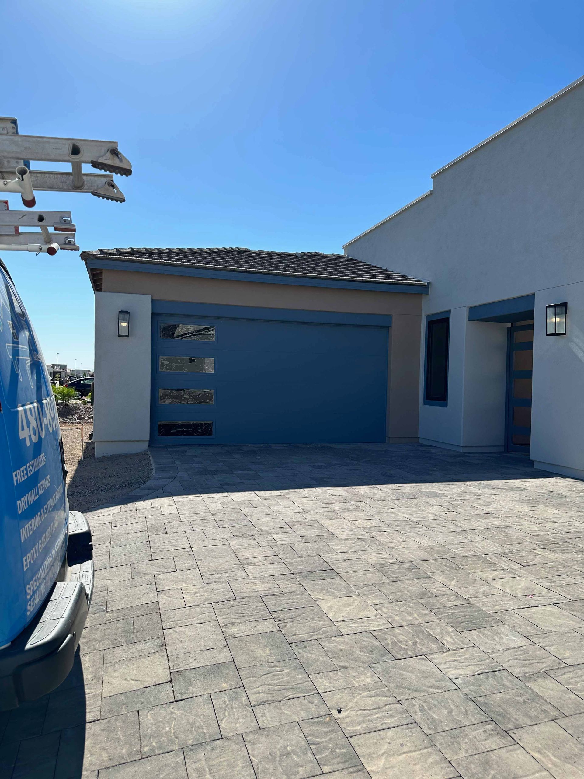 A blue van is parked in front of a white house with a blue garage door.