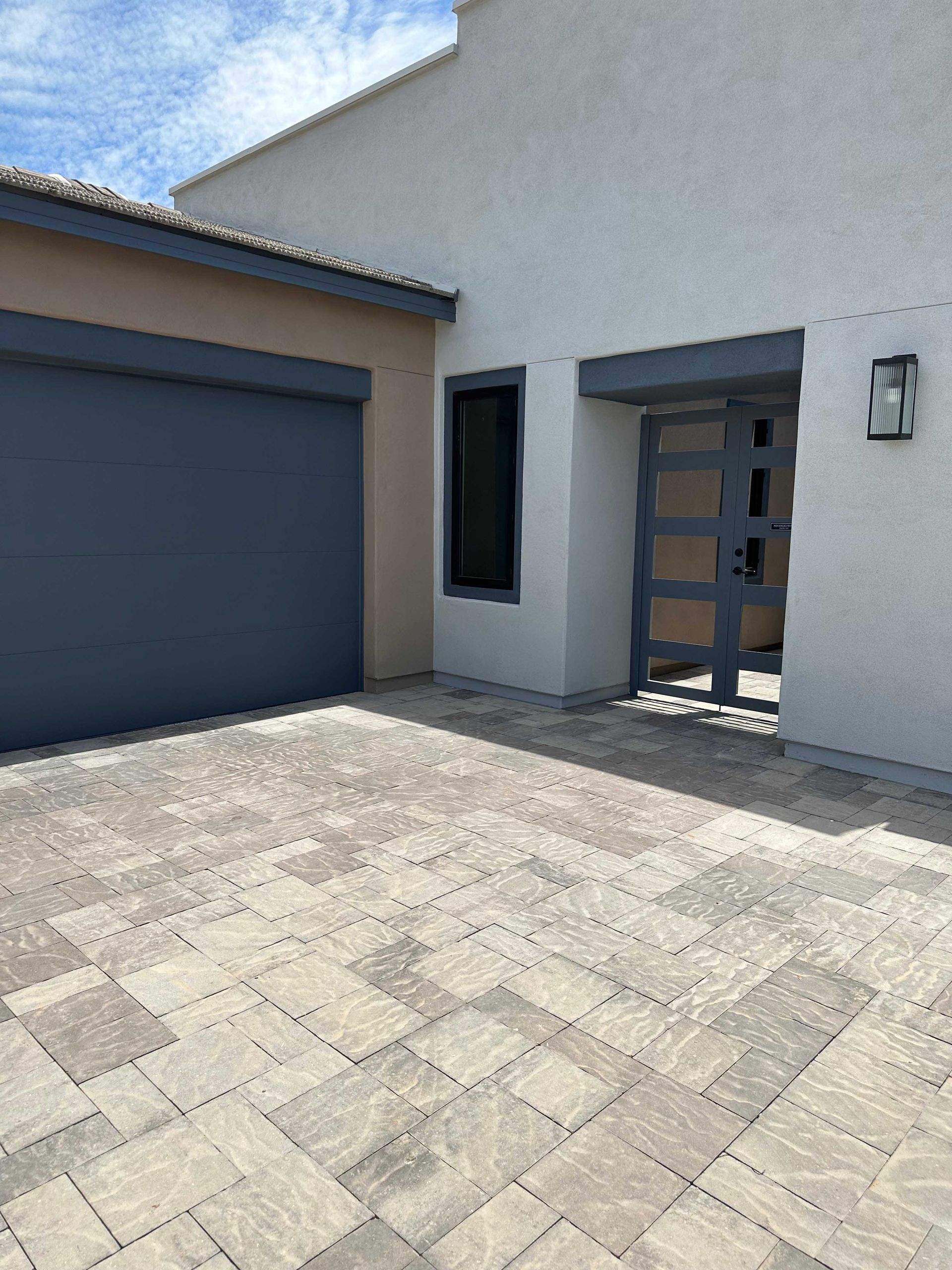 A white house with a blue garage door and a brick driveway.