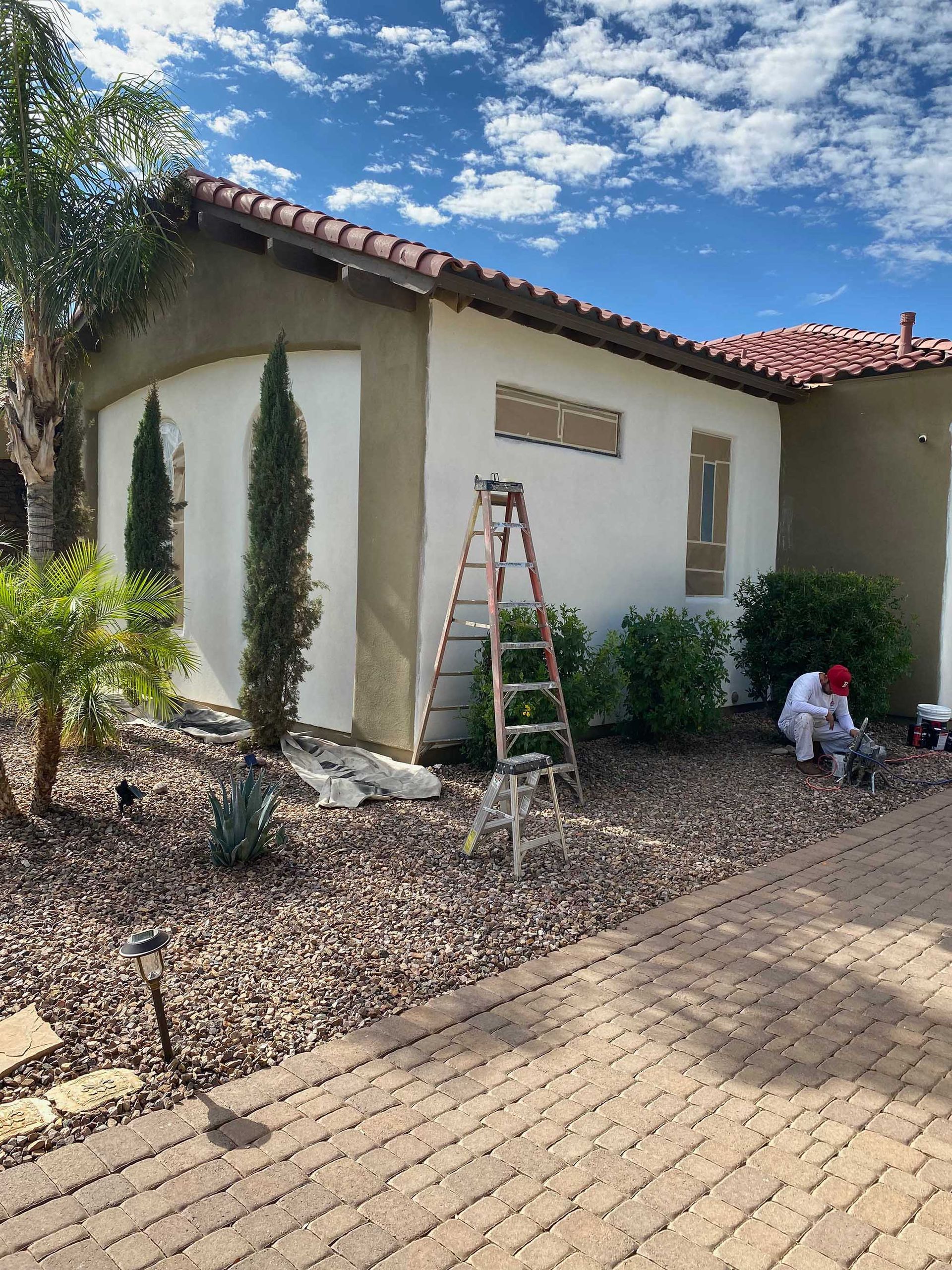 A man is painting the side of a house with a ladder.