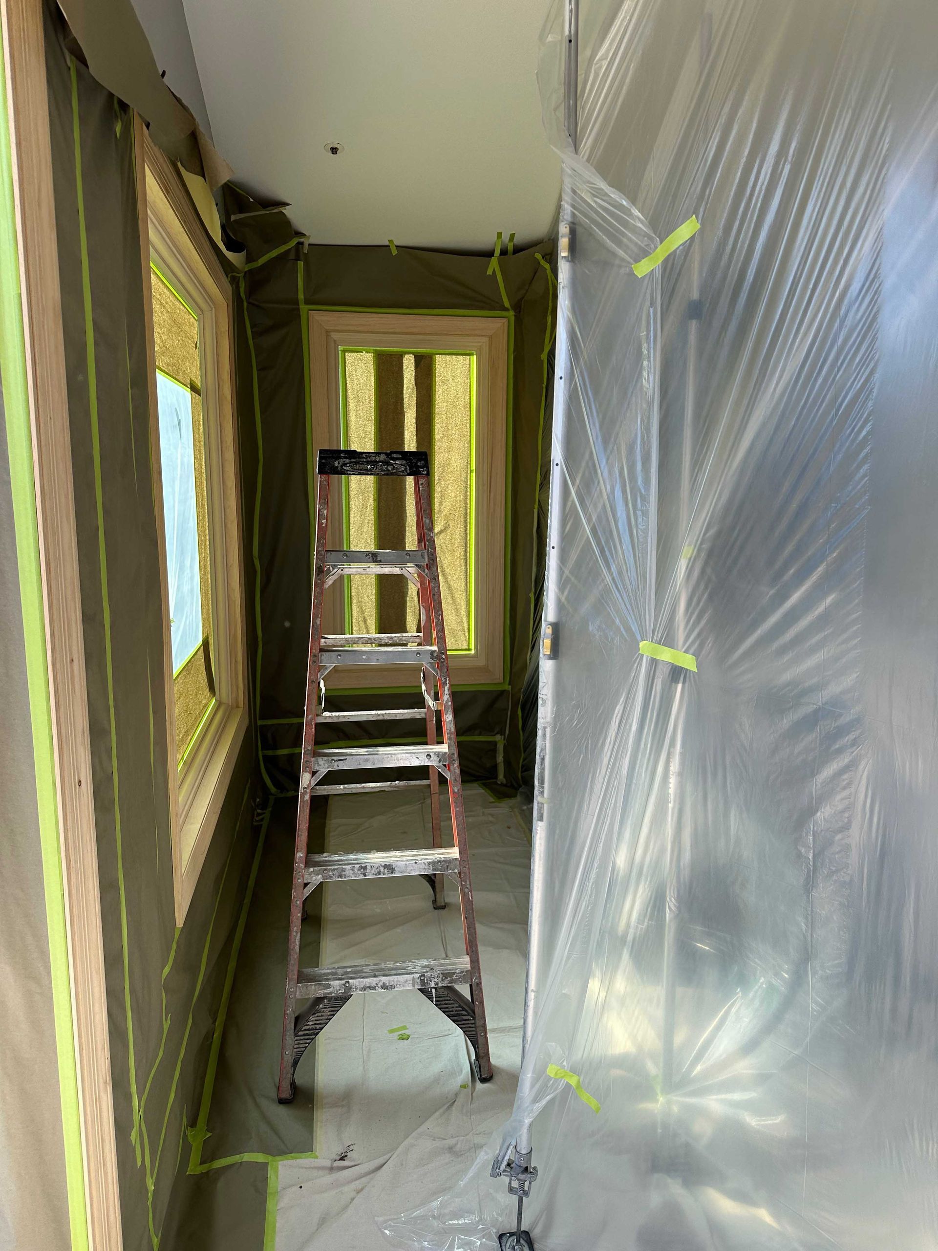 A ladder is sitting in a room covered in plastic.