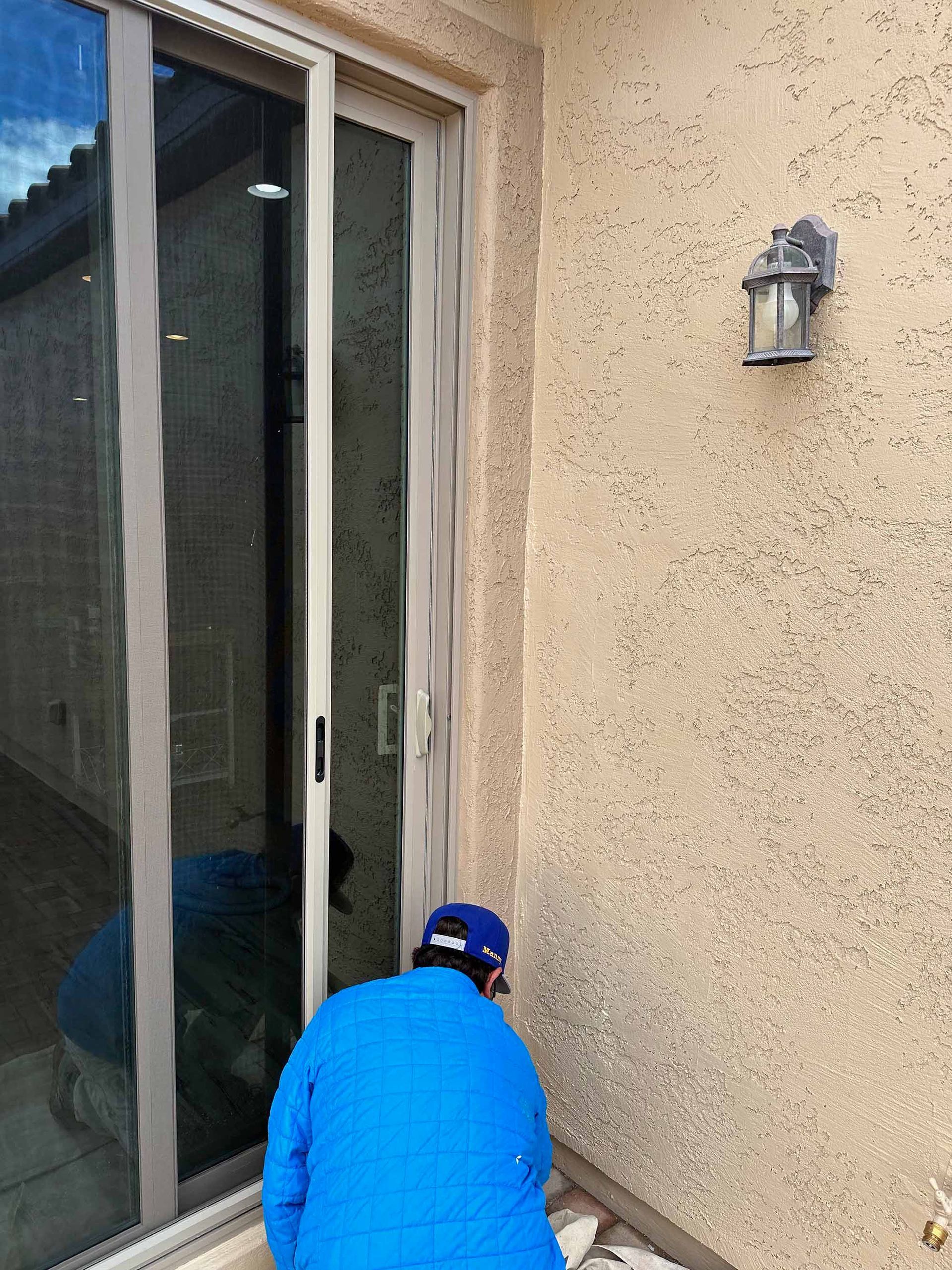 A man in a blue jacket is working on a sliding glass door.