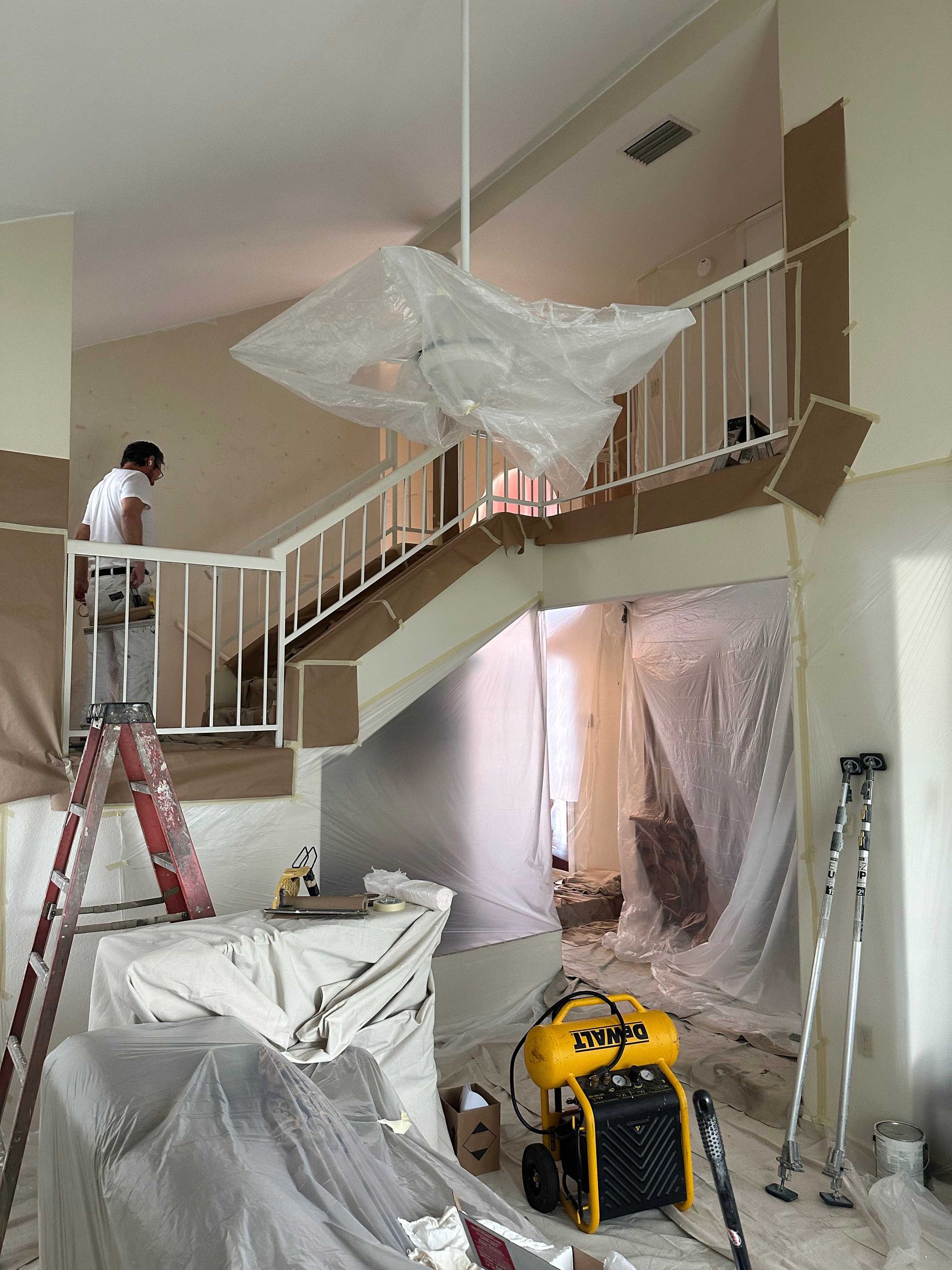 A man on a ladder is painting a wall in a house.