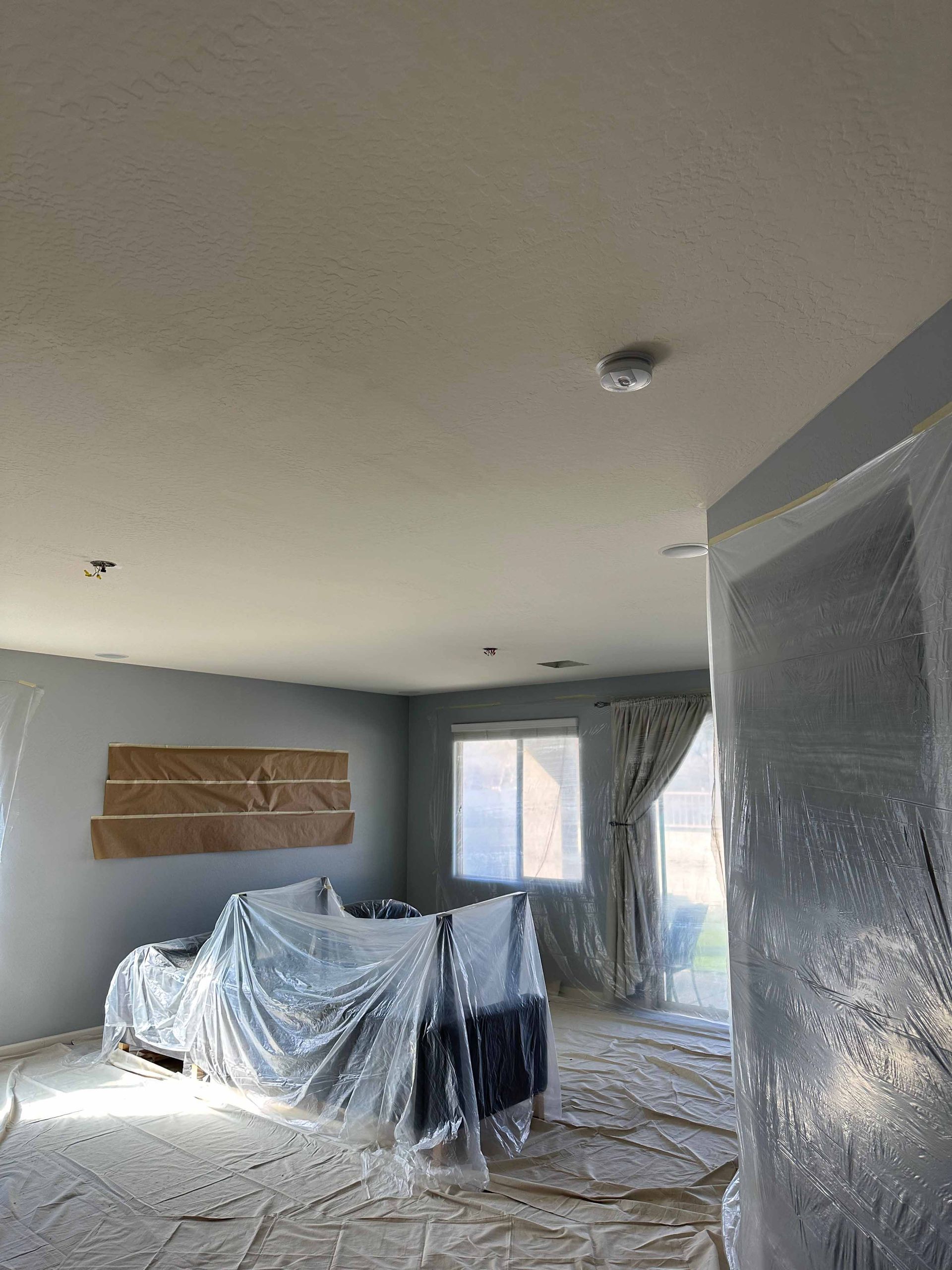 A living room is being painted and covered in plastic.