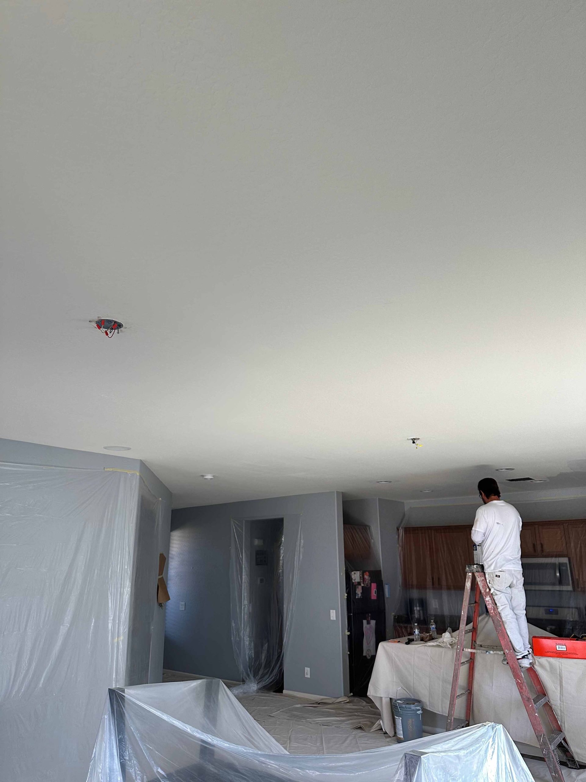A man is standing on a ladder in a living room painting the ceiling.
