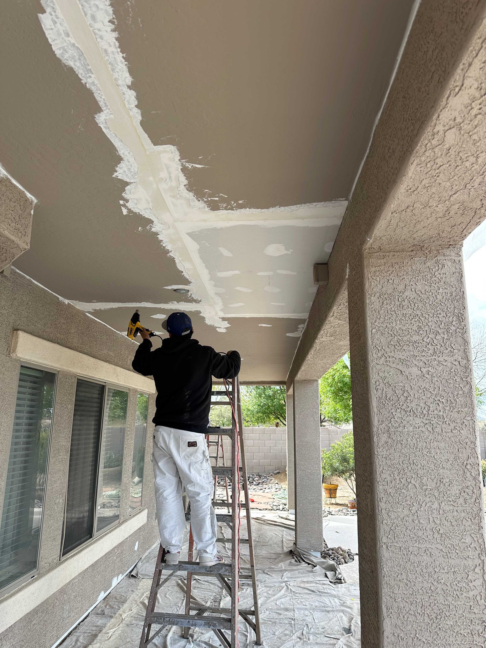 A man is standing on a ladder painting the ceiling of a building.
