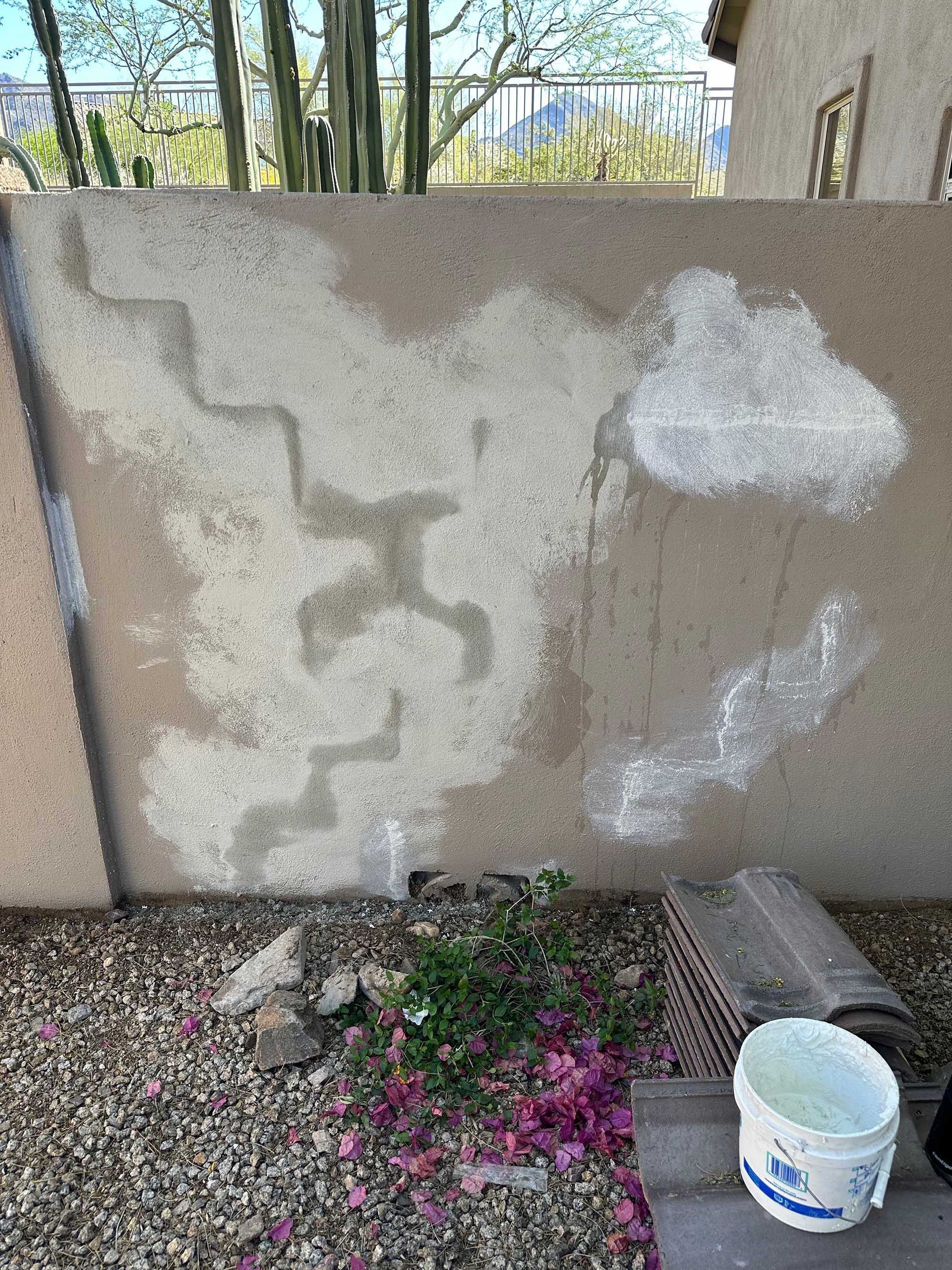A bucket of paint is sitting next to a concrete wall.