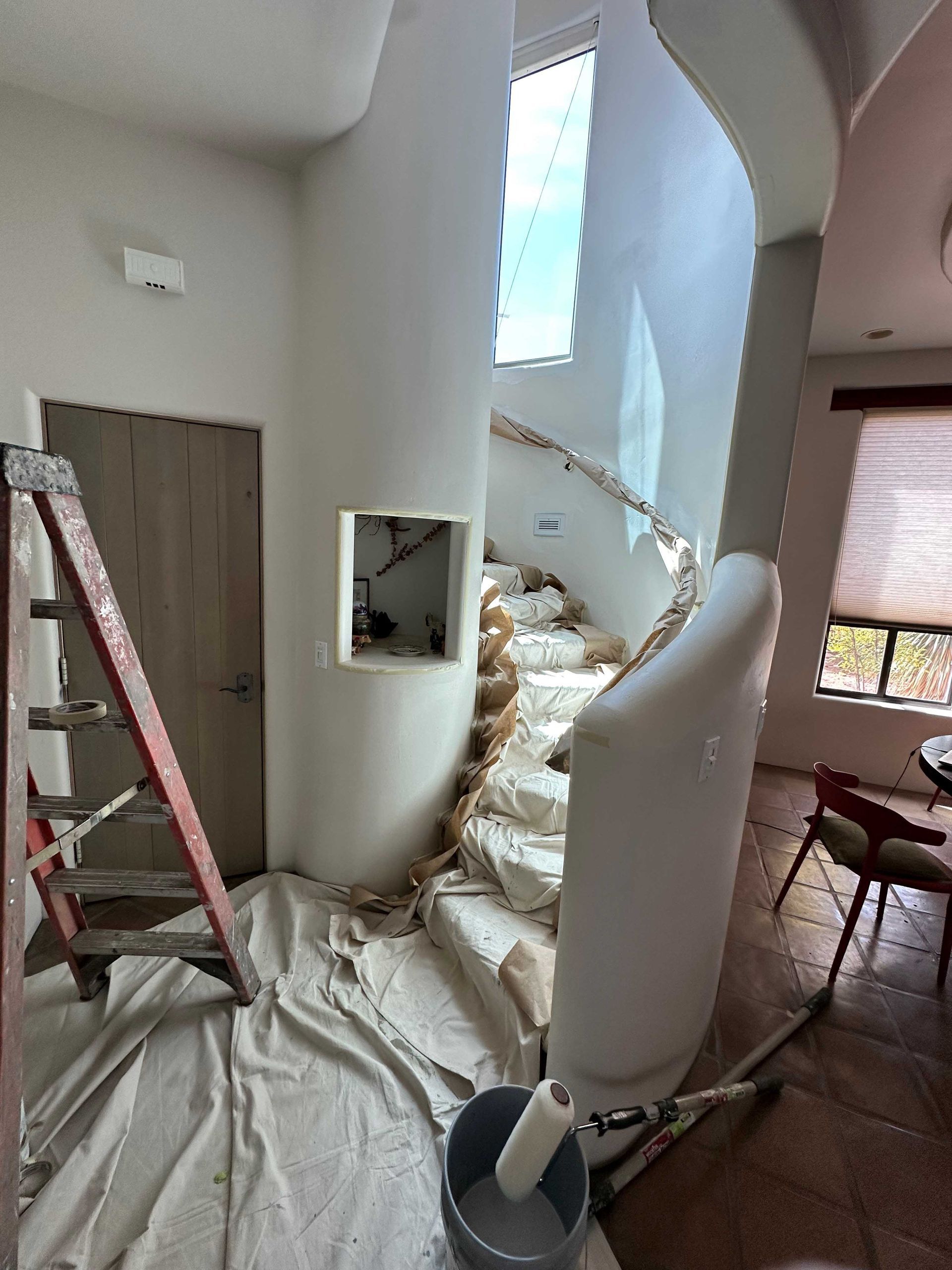 A staircase is being painted in a living room with a ladder.