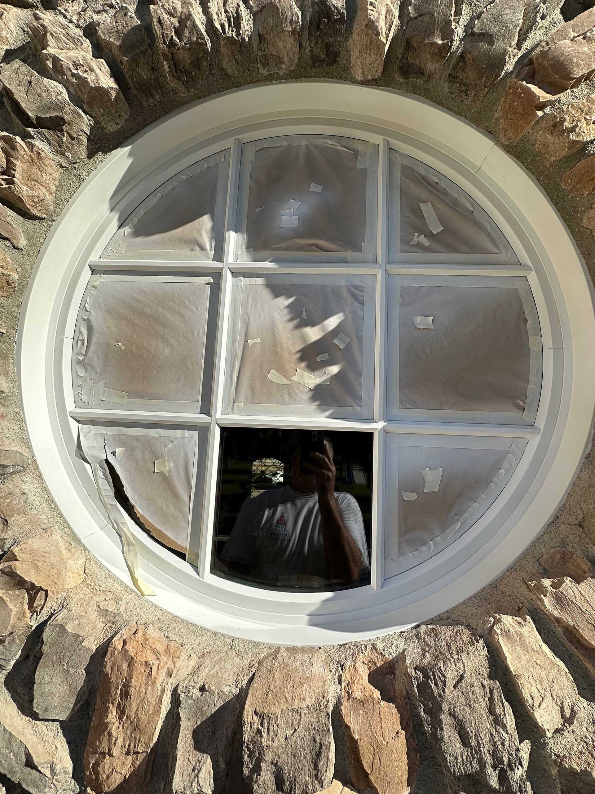 A man is taking a picture of himself in a round window in a stone wall.