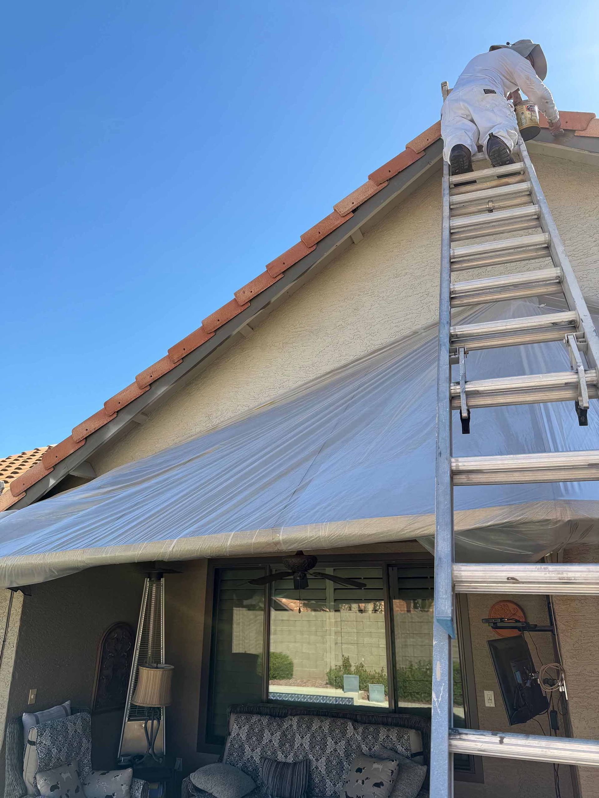 A man is standing on a ladder on the roof of a house.