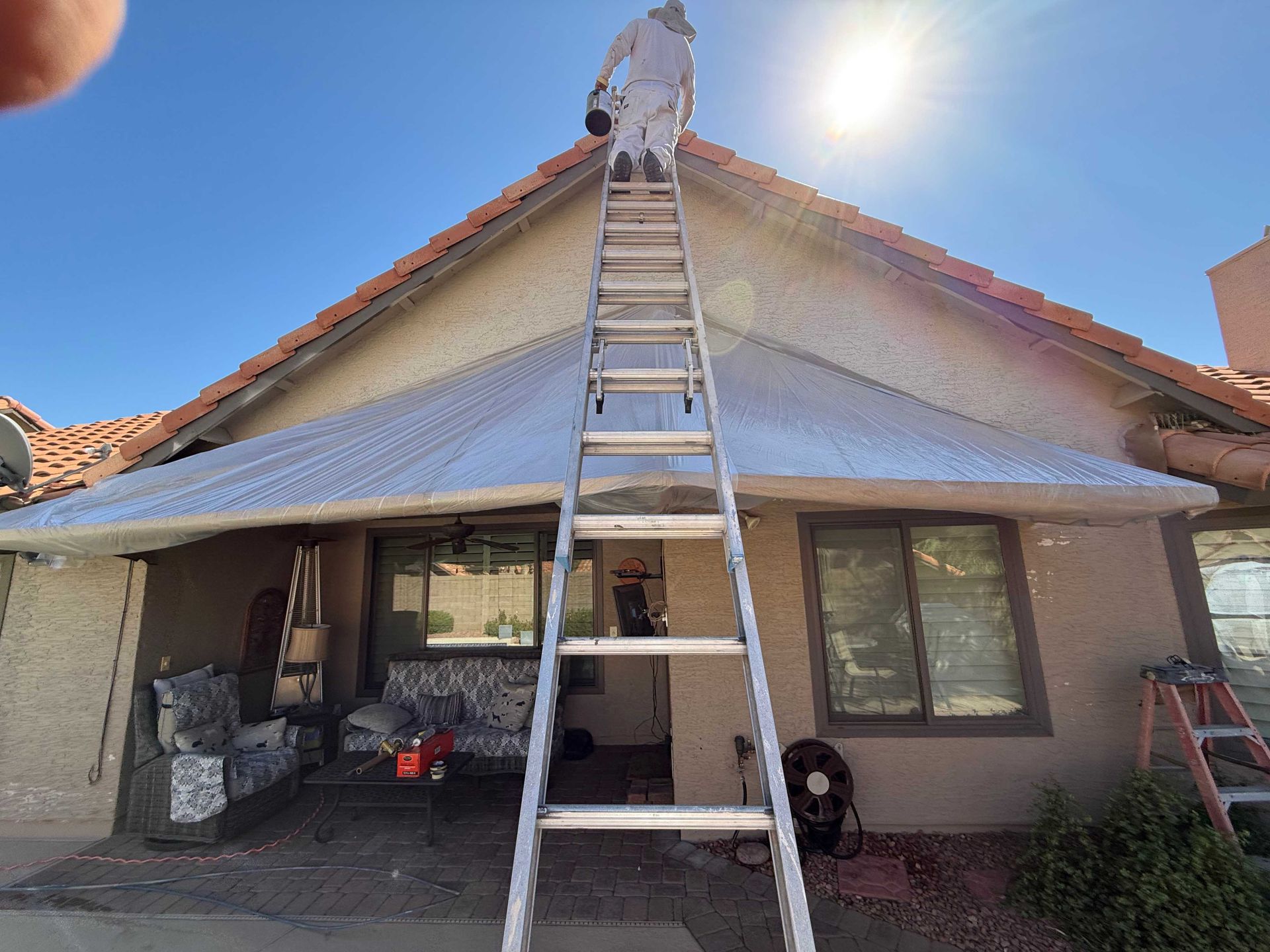 A man is standing on top of a ladder on the roof of a house.