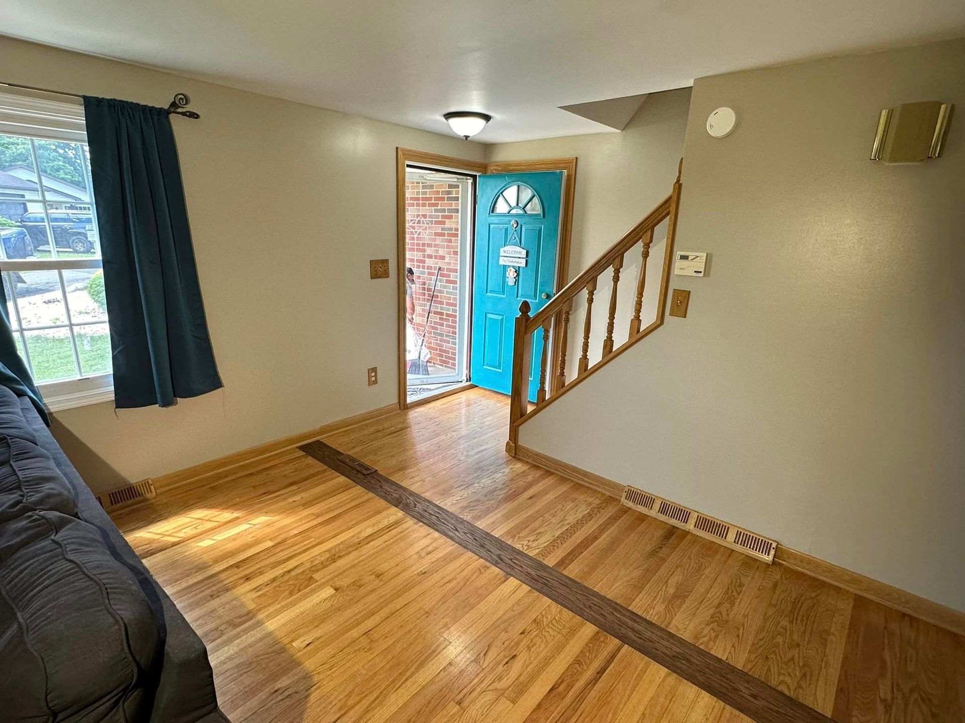 A living room with hardwood floors , a blue door and stairs.