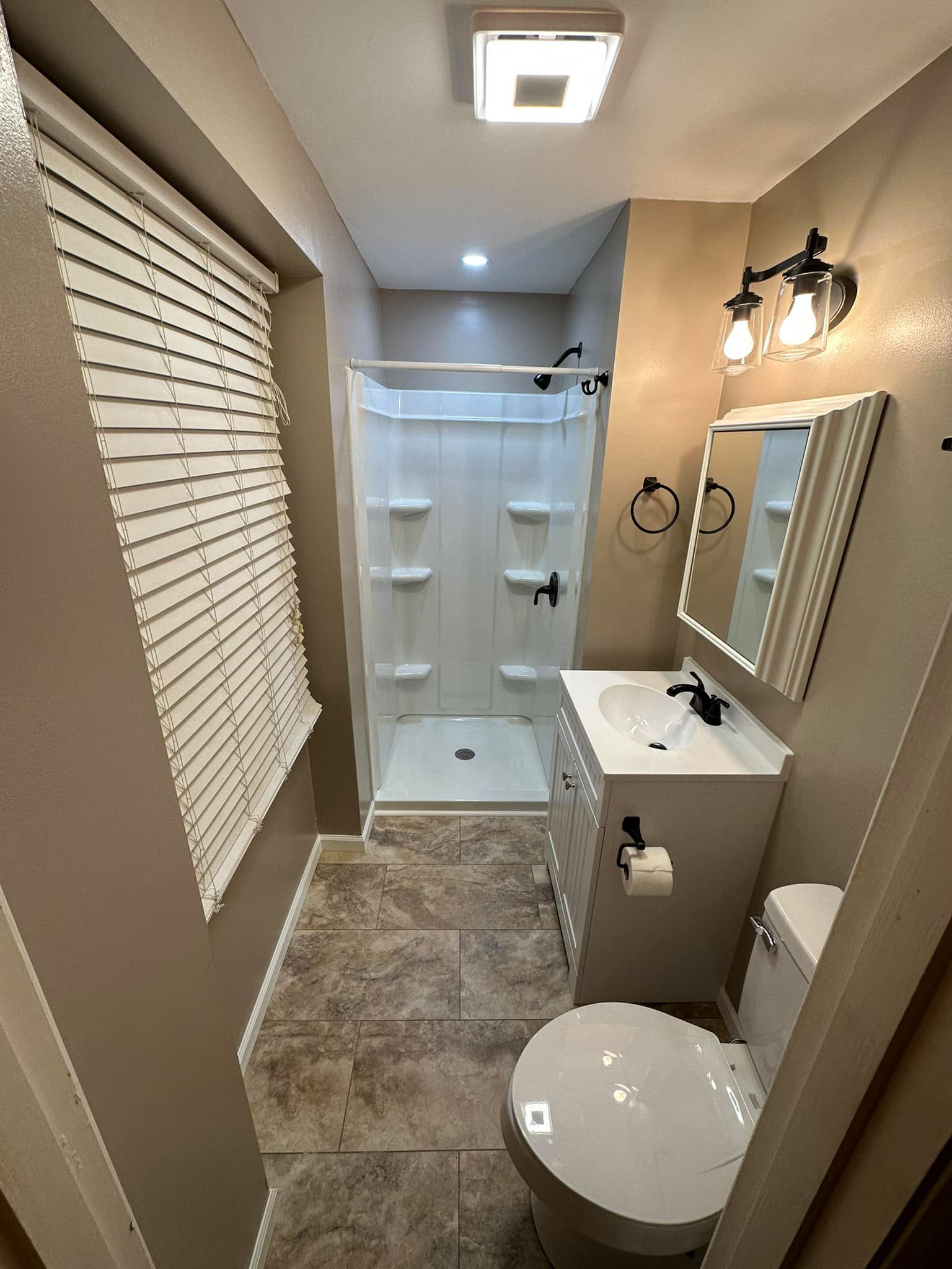 A bathroom with a toilet , sink , shower and mirror.