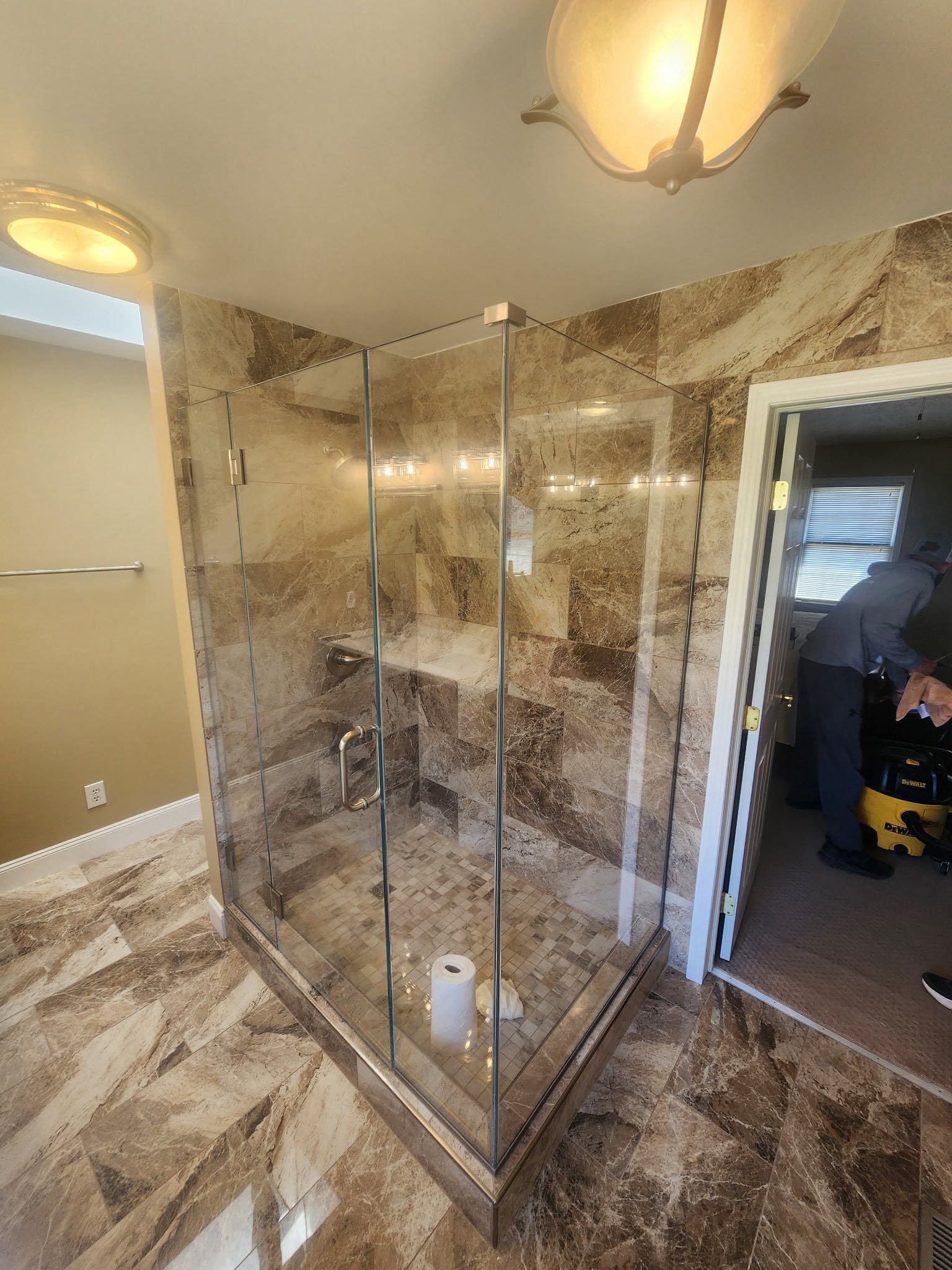 A man is working on a glass shower door in a bathroom.