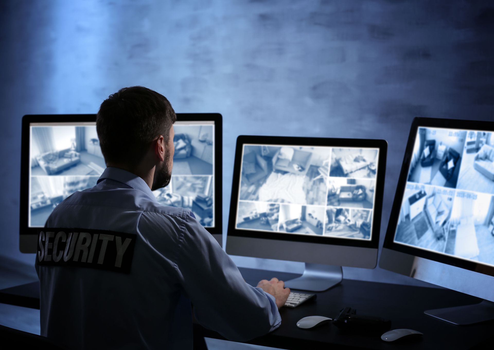 Security guard monitoring surveillance cameras on three computer screens in a dark control room