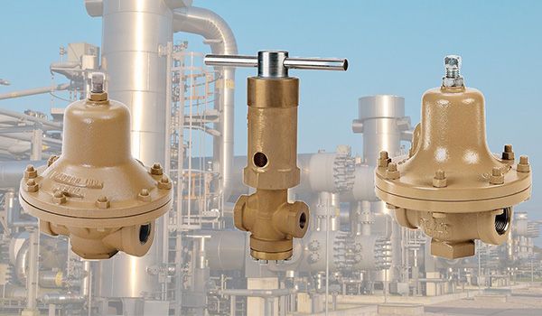 Three industrial pressure regulator valves on a background of factory equipment.