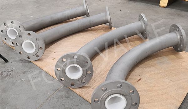 Four curved pipes with white ceramic lining and flanged ends, lying on wood.