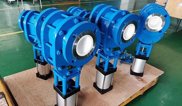 Blue industrial valves on silver supports, stacked on a wooden pallet in a factory.