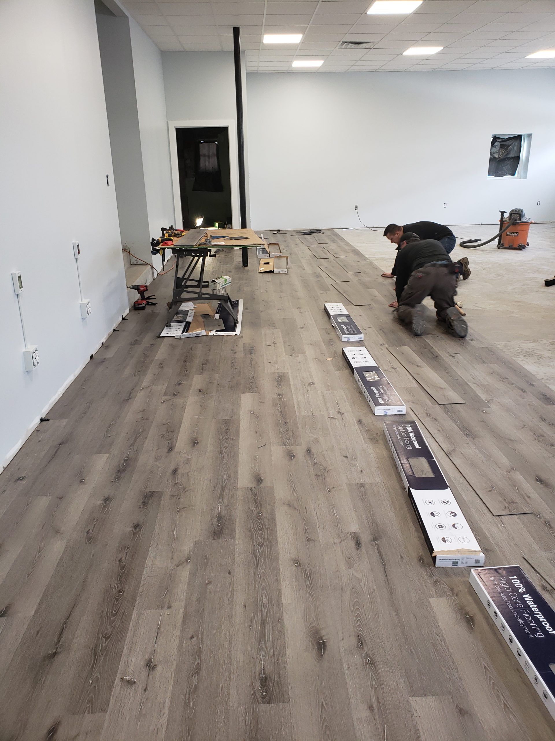 Men installing wood-look flooring in a room. Tools and boxes of flooring are present.